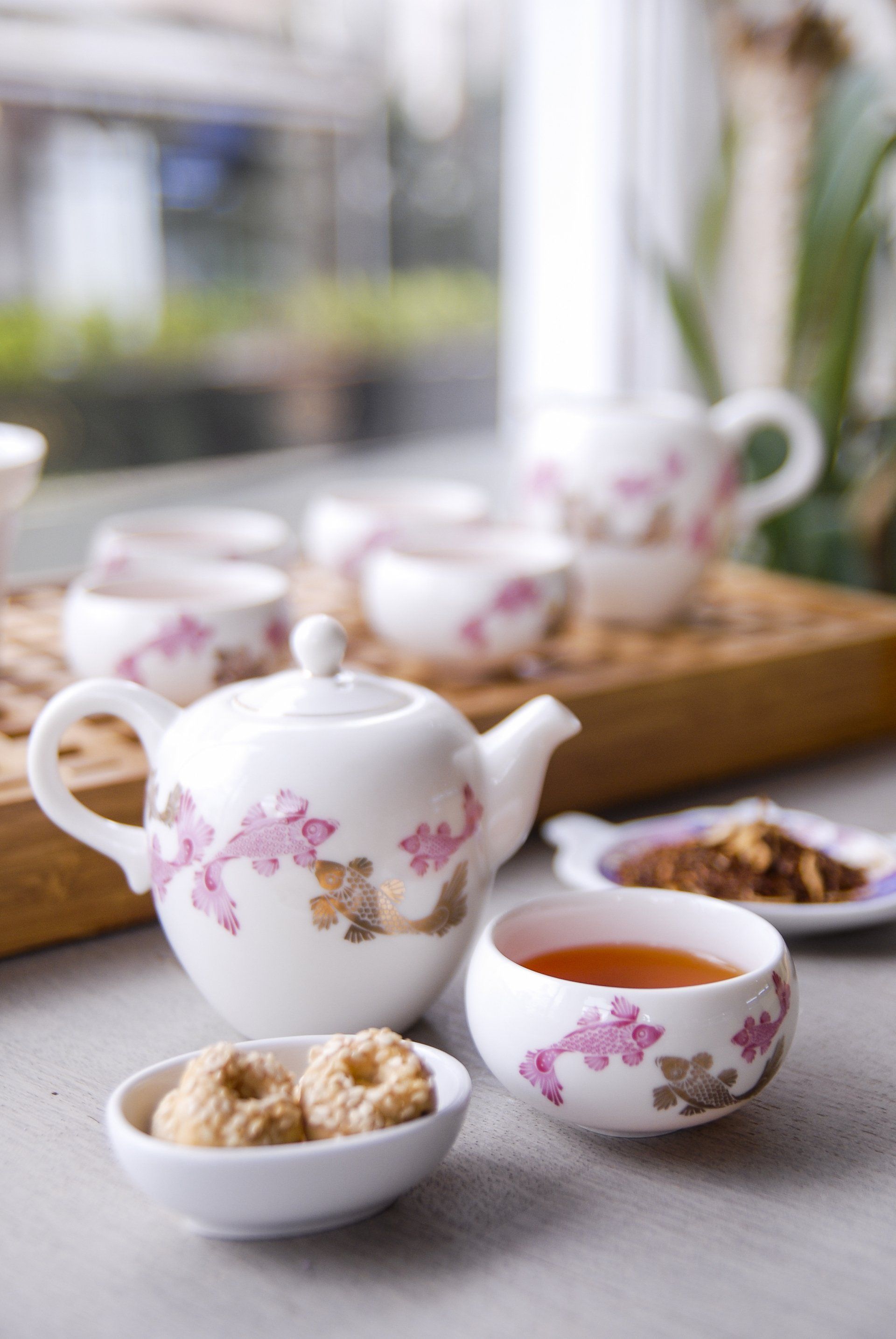 Tea set with teapot, cup, small bowl with cookies, and tea leaves on a wooden tray.