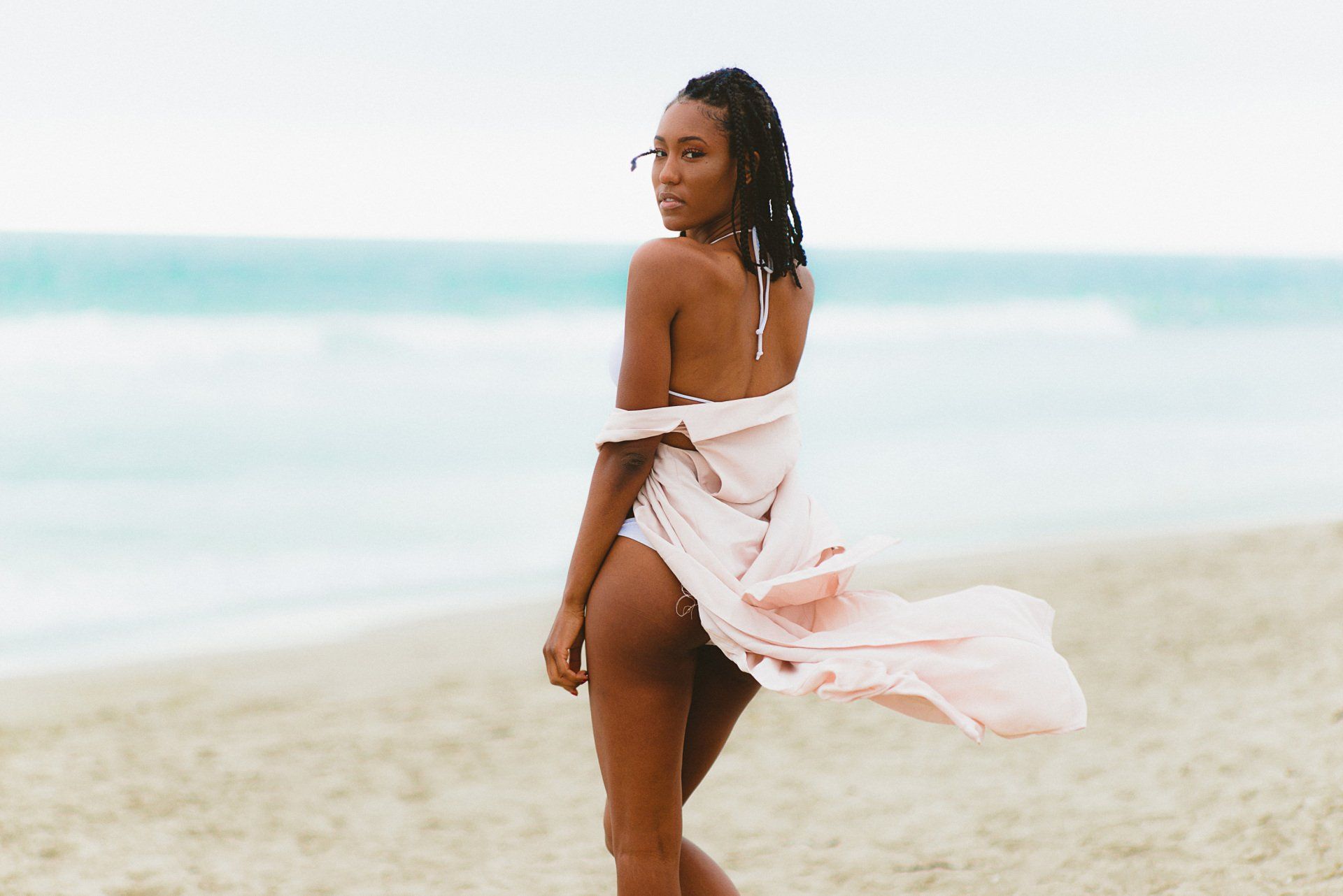 A woman in a pink dress is standing on a beach.