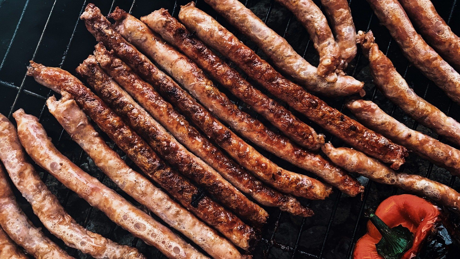 Grilled sausages on a black grill with a red pepper.