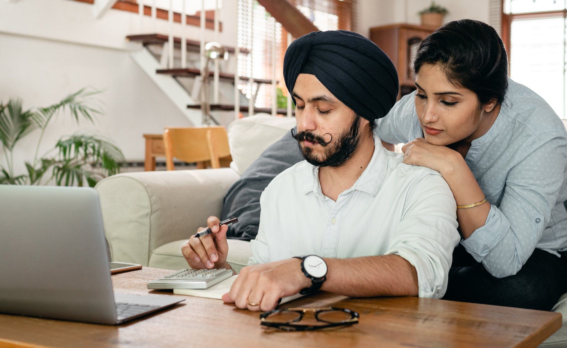A man and a woman are sitting at a table looking at a laptop.