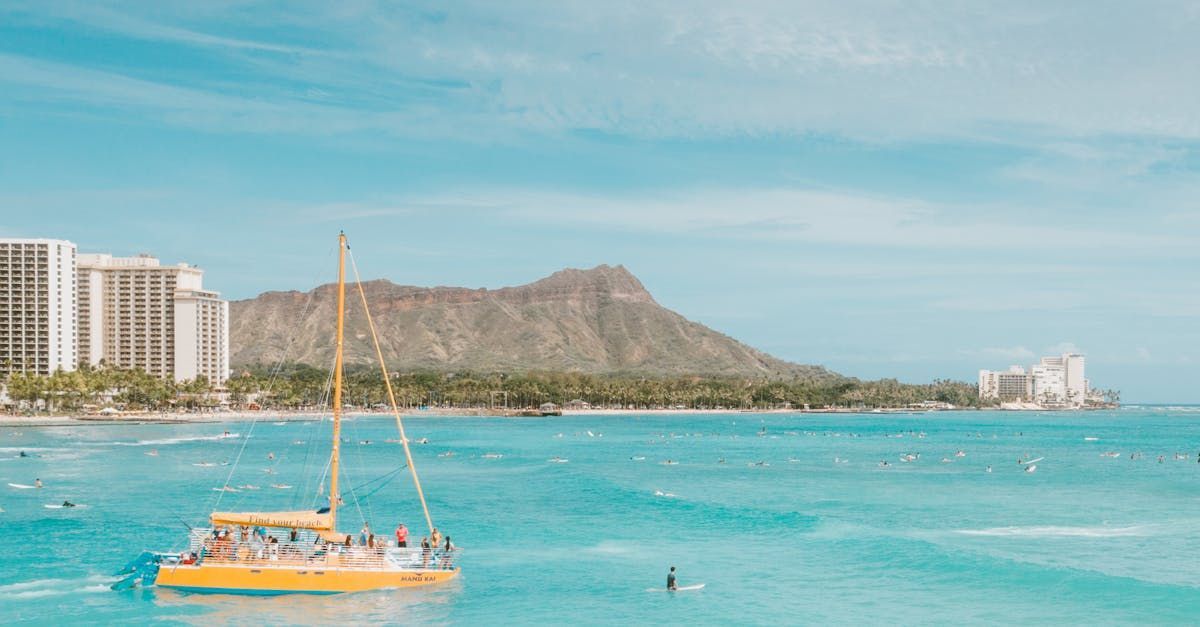 A yellow sailboat is floating in the ocean with a mountain in the background.