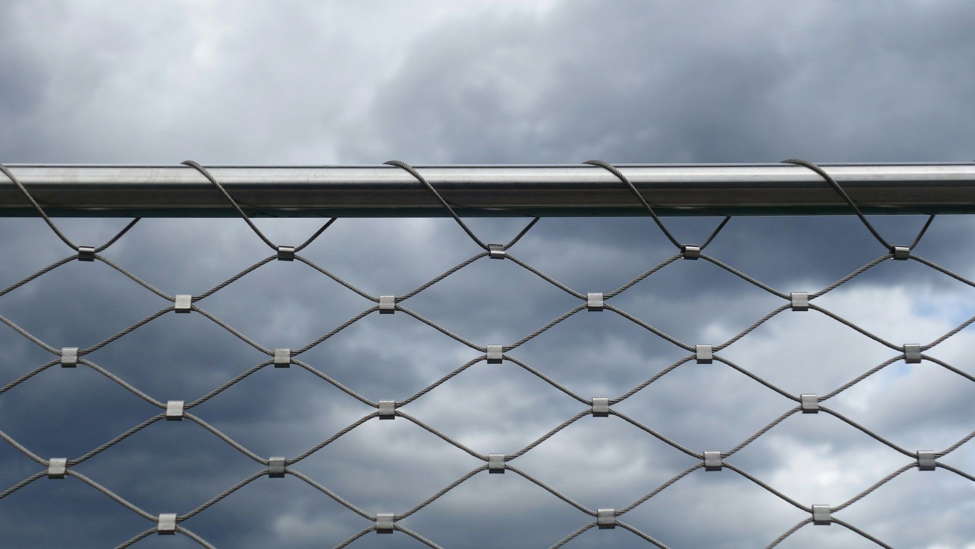 A close up of a chain link fence with a cloudy sky in the background.