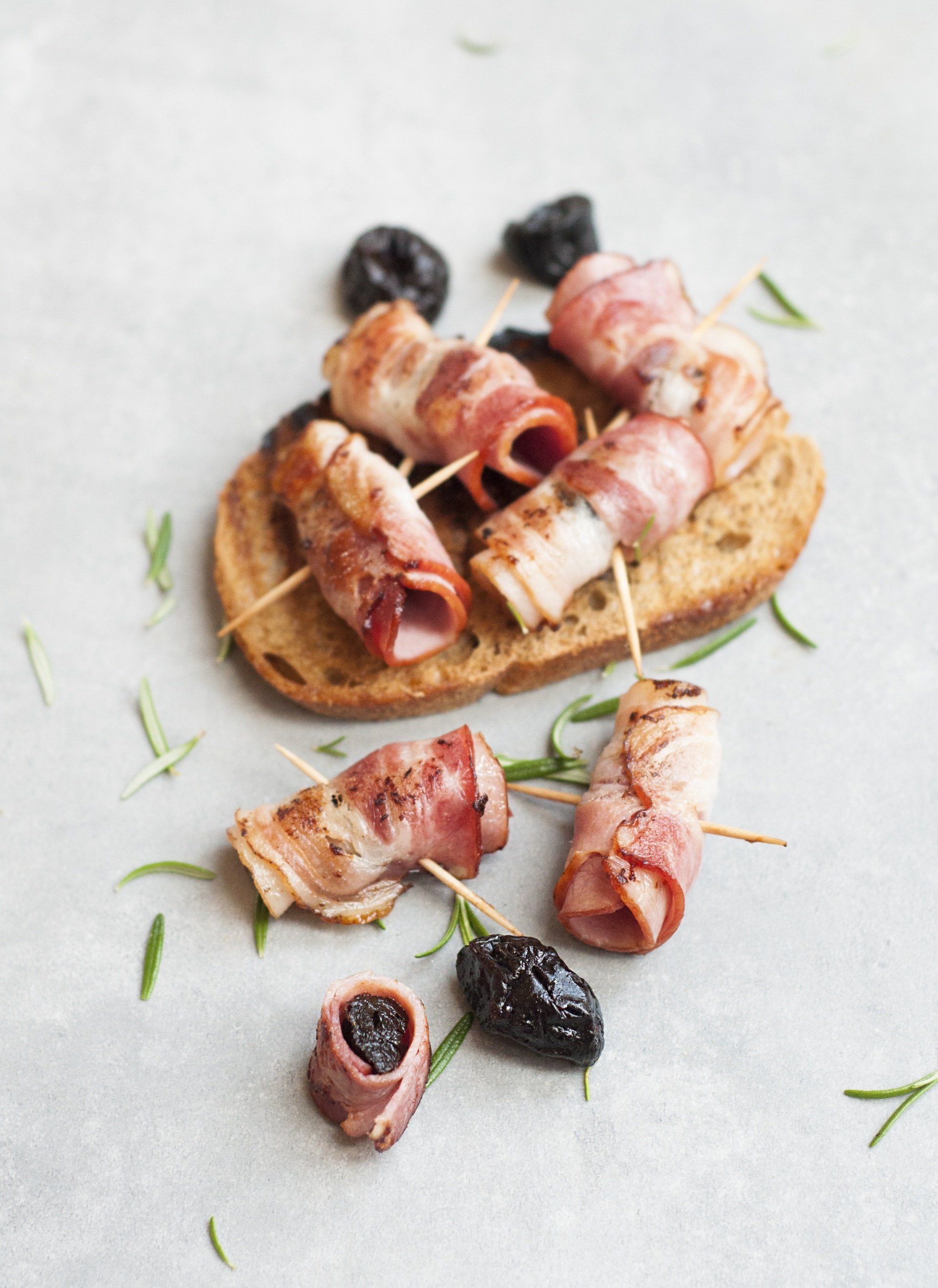 A close up of bacon wrapped olives on a piece of bread on a table.
