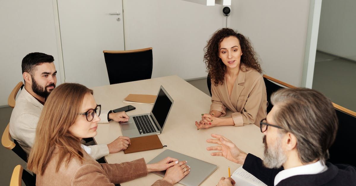 A group of people are sitting around a table with laptops.