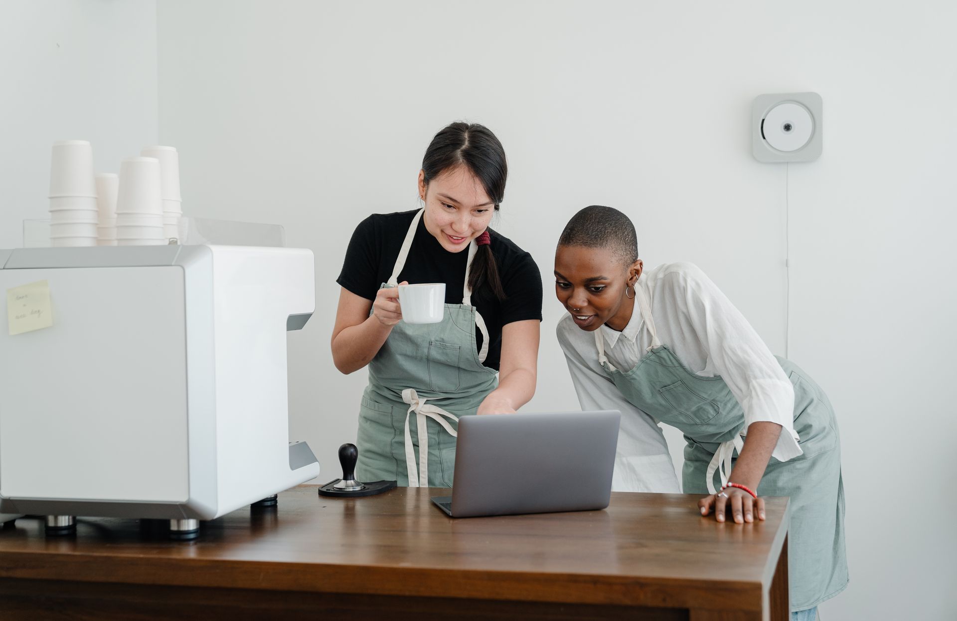 Two women are standing at a table looking at a laptop.