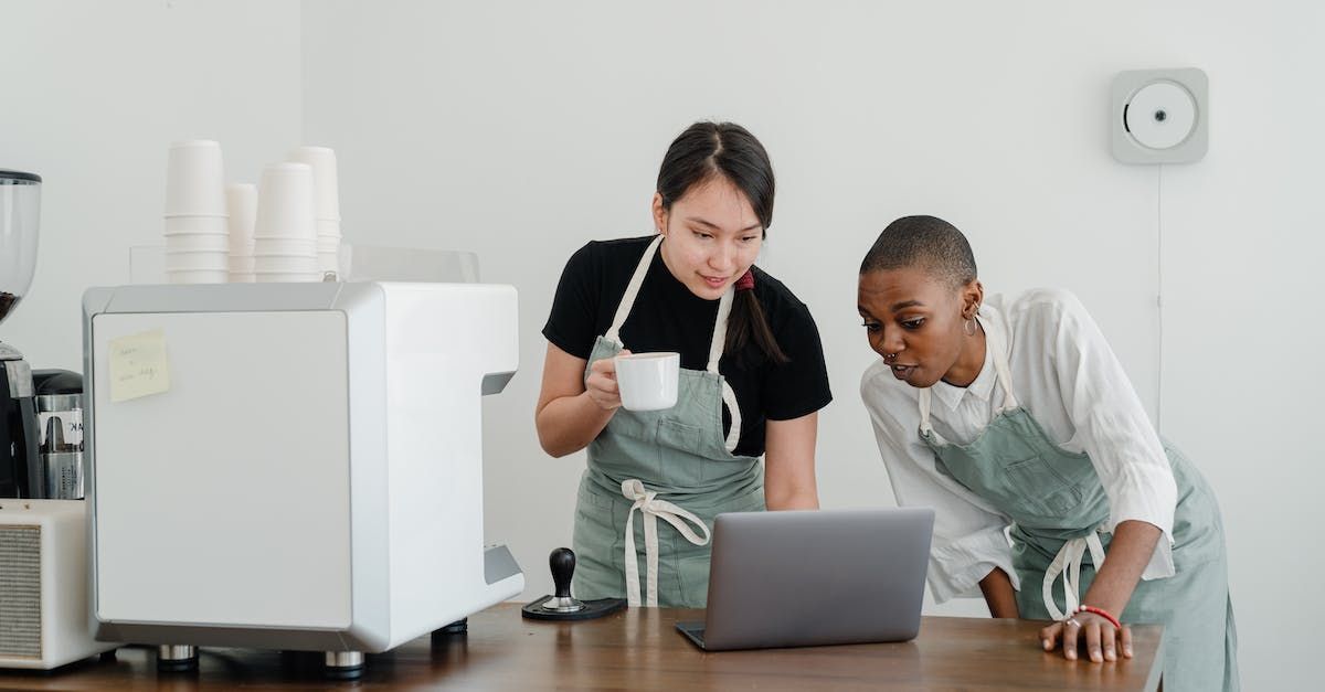 Two women are standing at a table looking at a laptop.