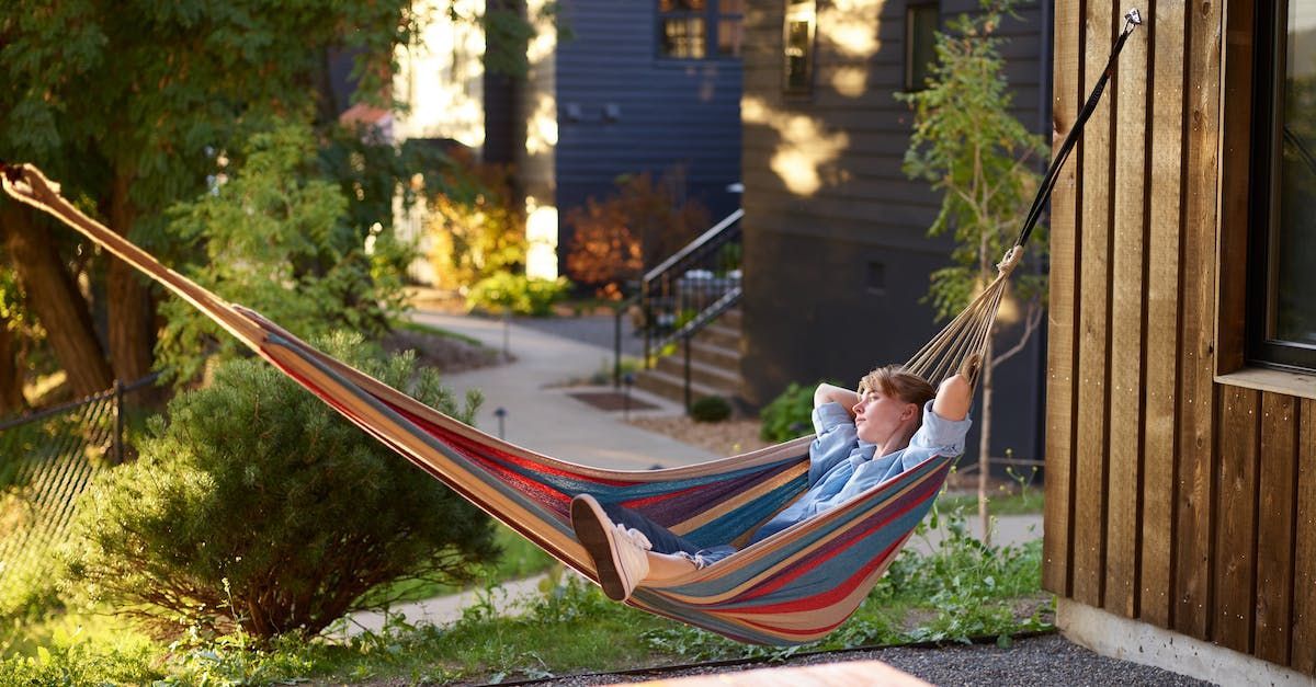 A man is laying in a hammock outside of a house.