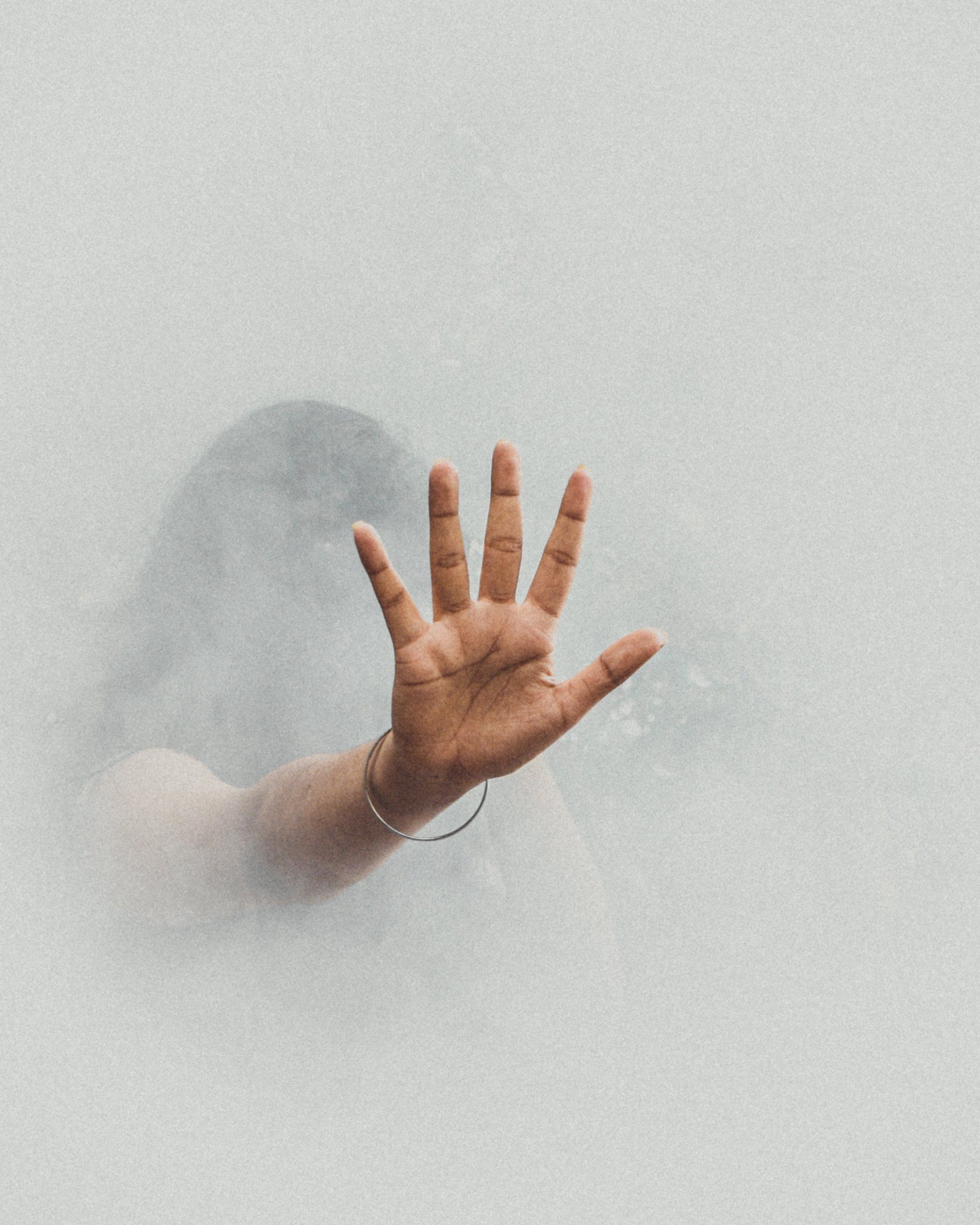 A hand extends forward with an open palm through a textured, light gray misty background.