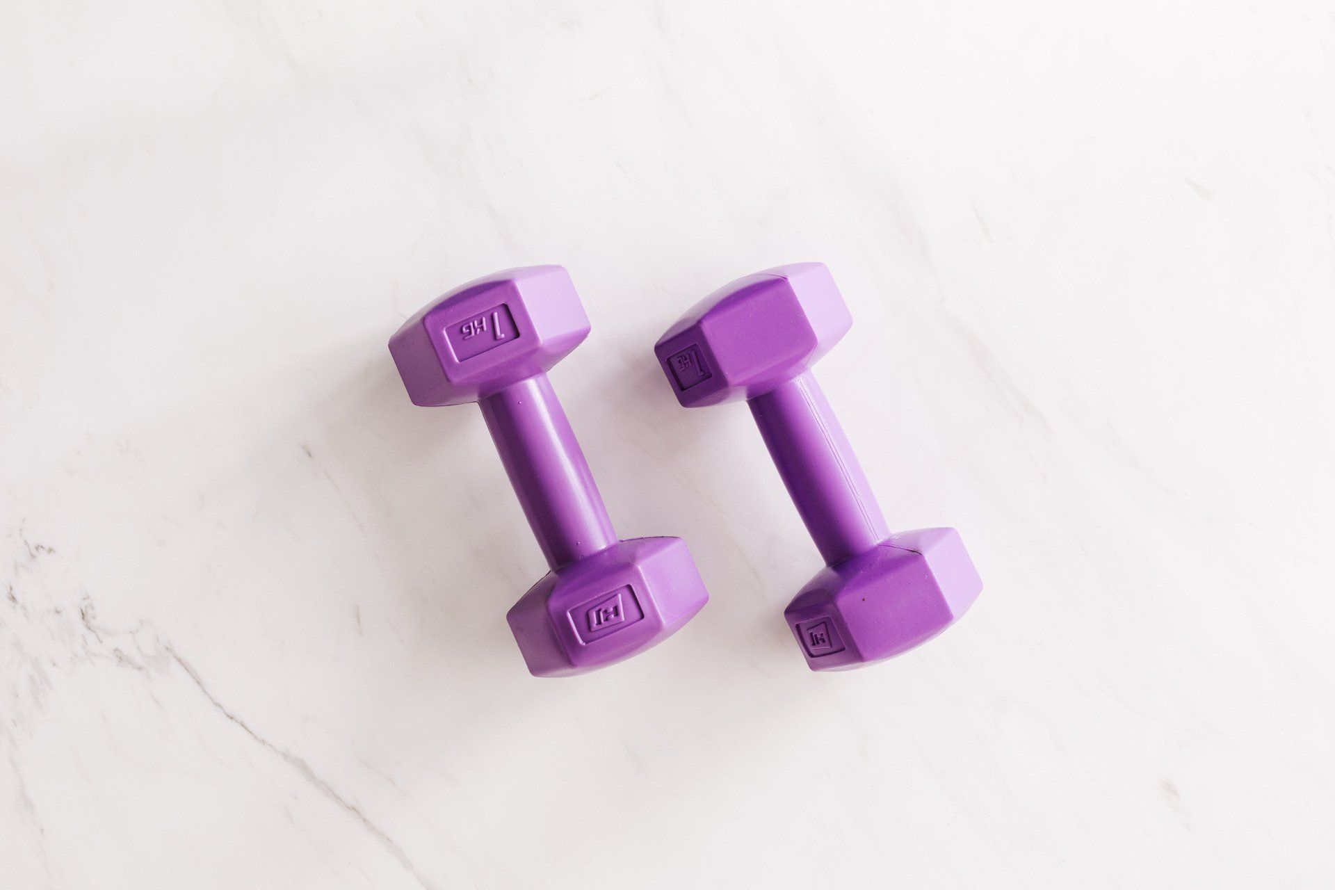 Two purple dumbbells are sitting on a white surface.
