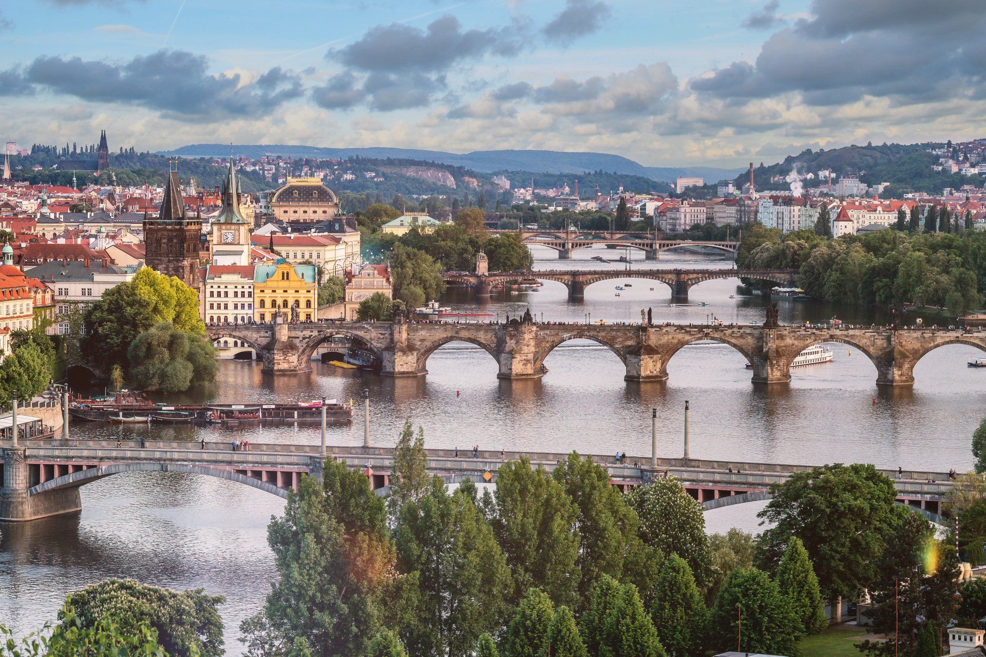 Panoramic cityscape with bridges over a river at dusk, featuring colorful buildings and a domed landmark.