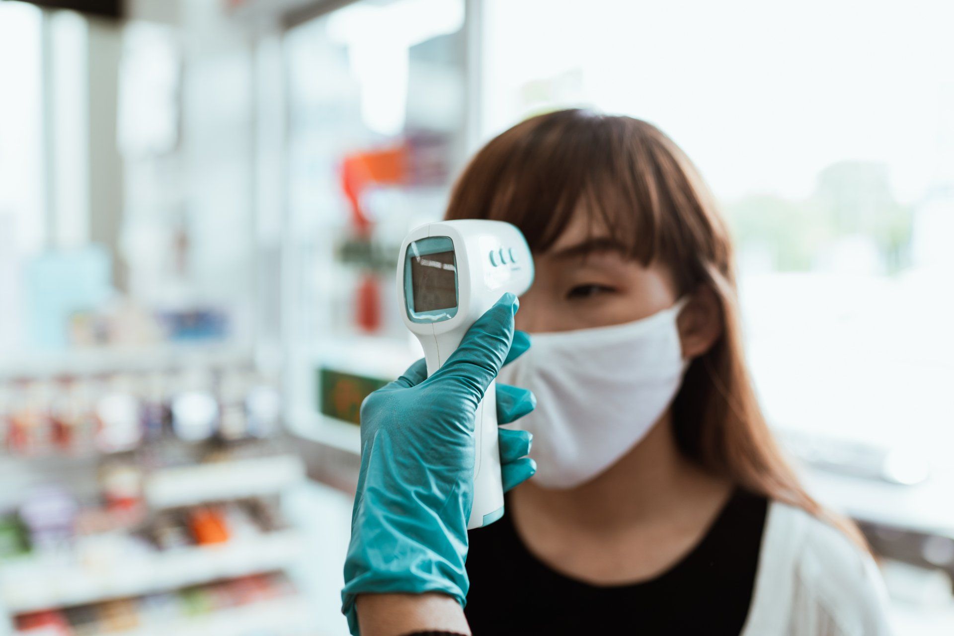 A gloved hand holds a forehead thermometer to a woman's head