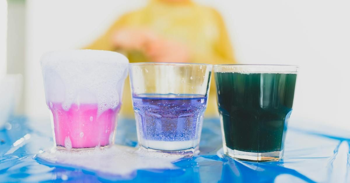 Three glasses of different colored liquids are sitting on a table.