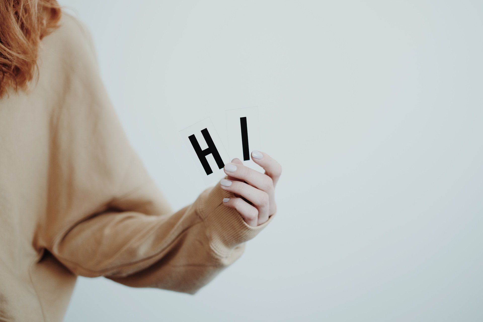 A woman in a tan sweater is holding the letters hi in her hands