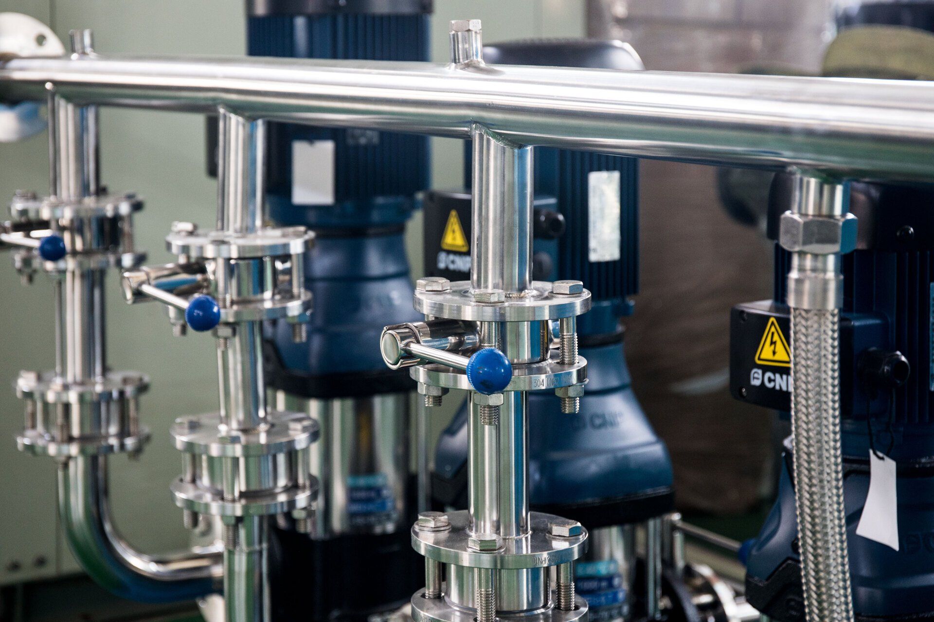 A row of stainless steel pipes and pumps in a factory.