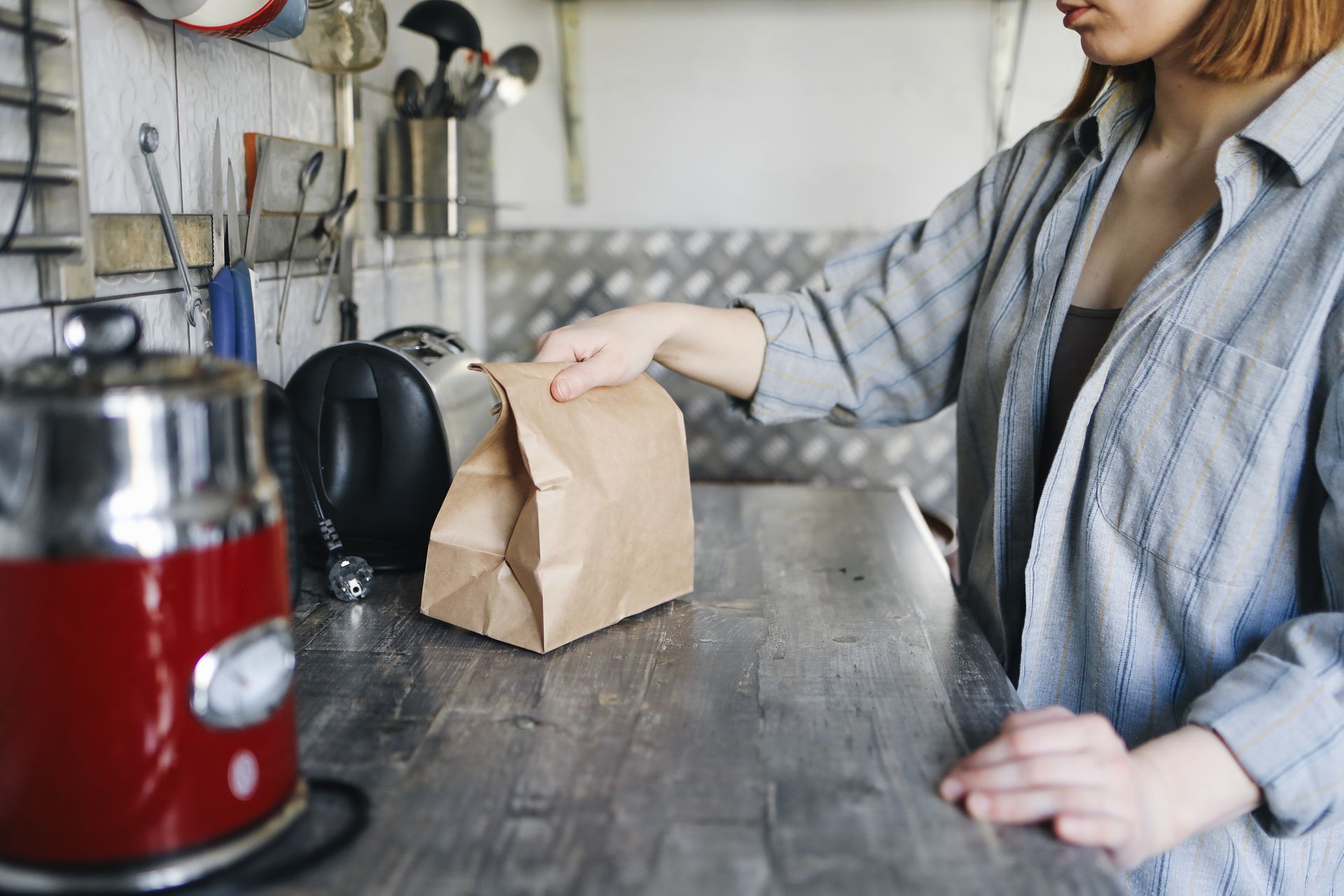A woman is holding a brown paper bag on a kitchen counter.