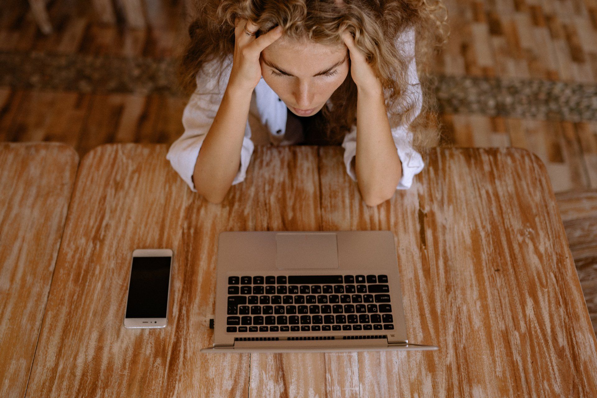 A woman is sitting at a table with a laptop and a cell phone.
