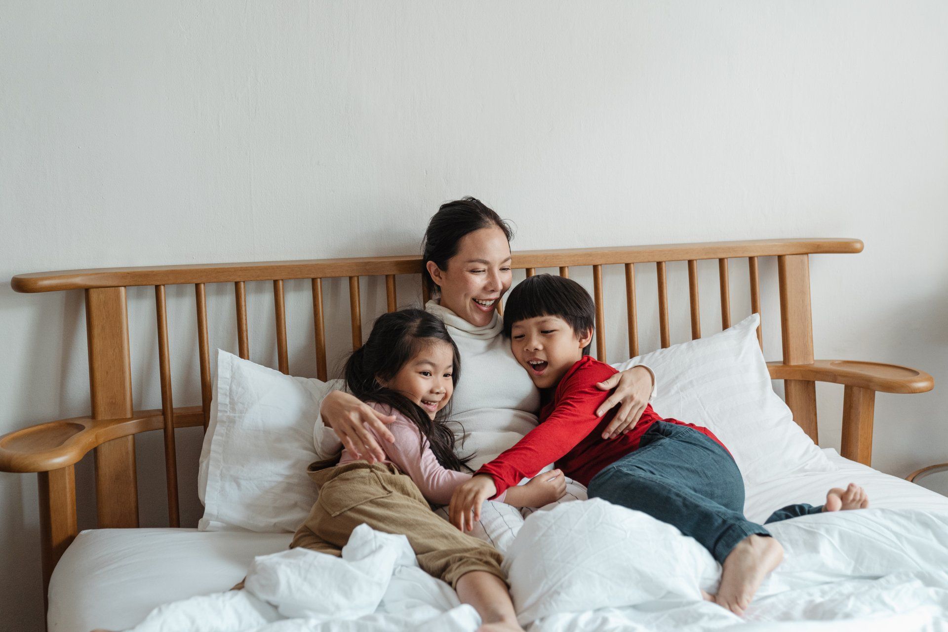A mother lies in bed with her daughter and son. They are hugging each other and sharing a laugh.