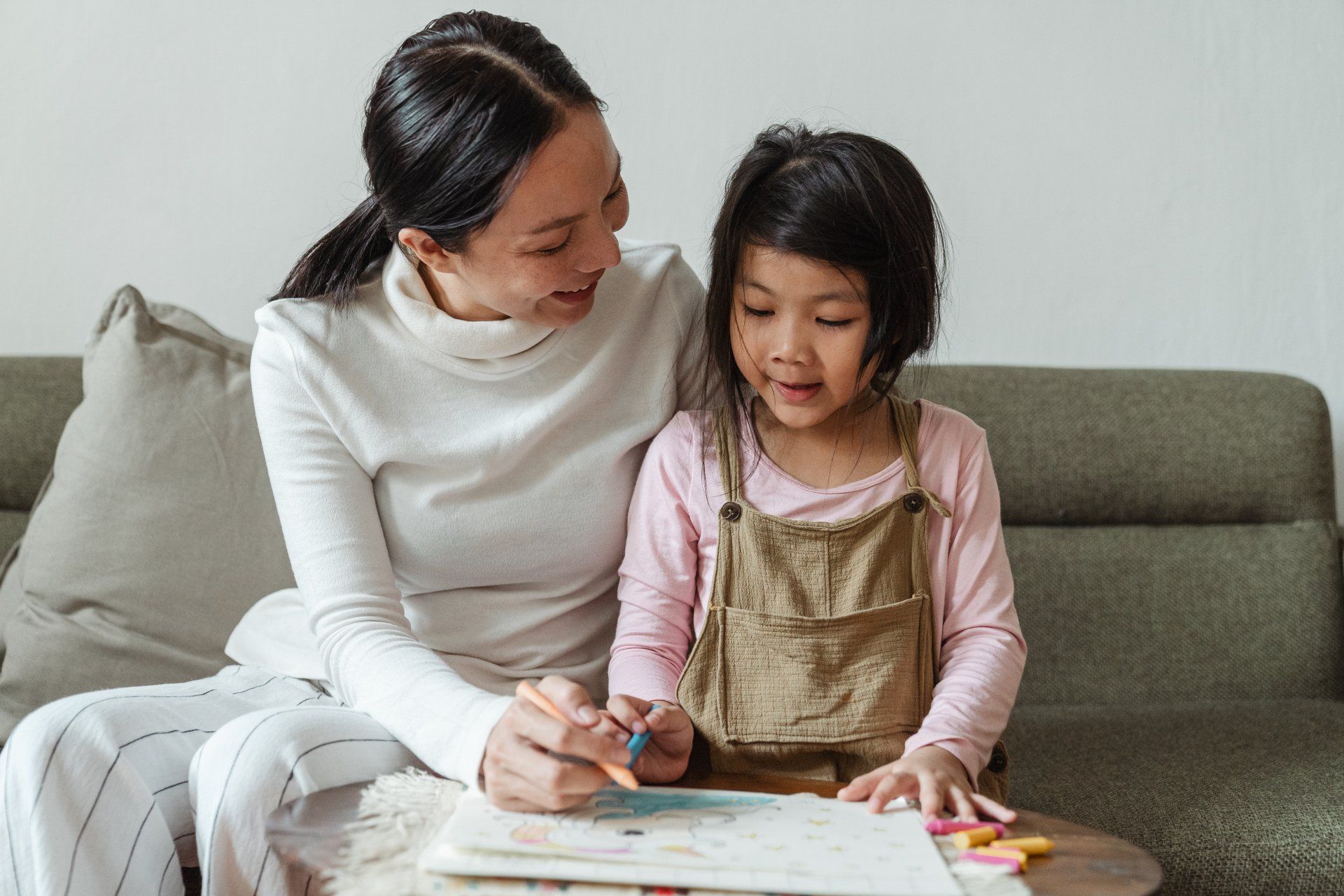 Woman and child sitting on a couch, drawing together with crayons on a sheet of paper