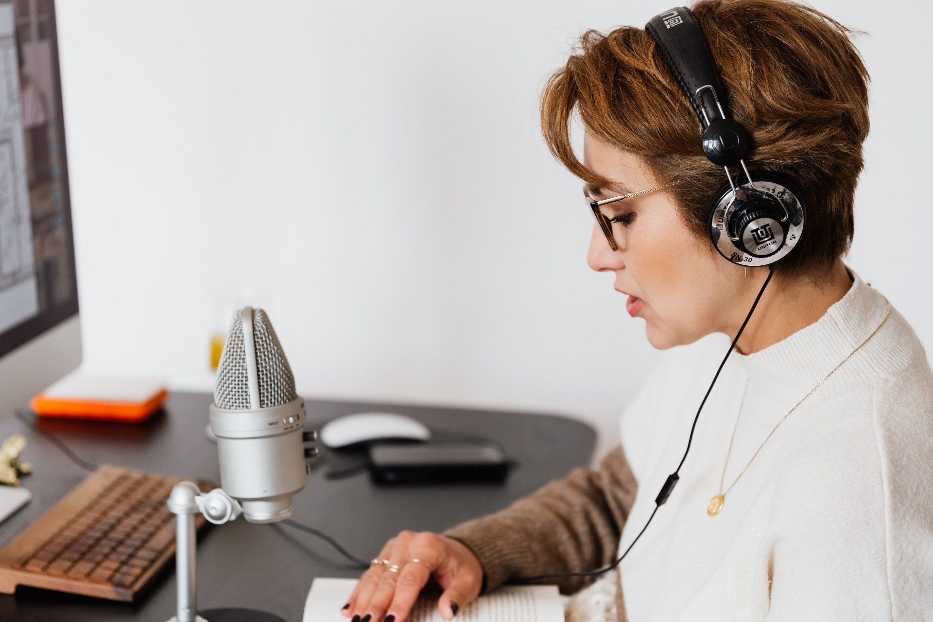 A woman wearing headphones is sitting at a desk in front of a microphone.