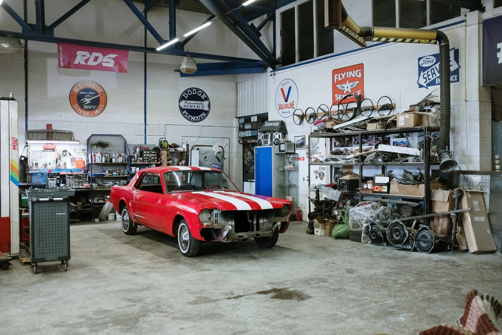 Red car with white stripes in a cluttered garage with spare parts and tools | 5 Star Auto Repair