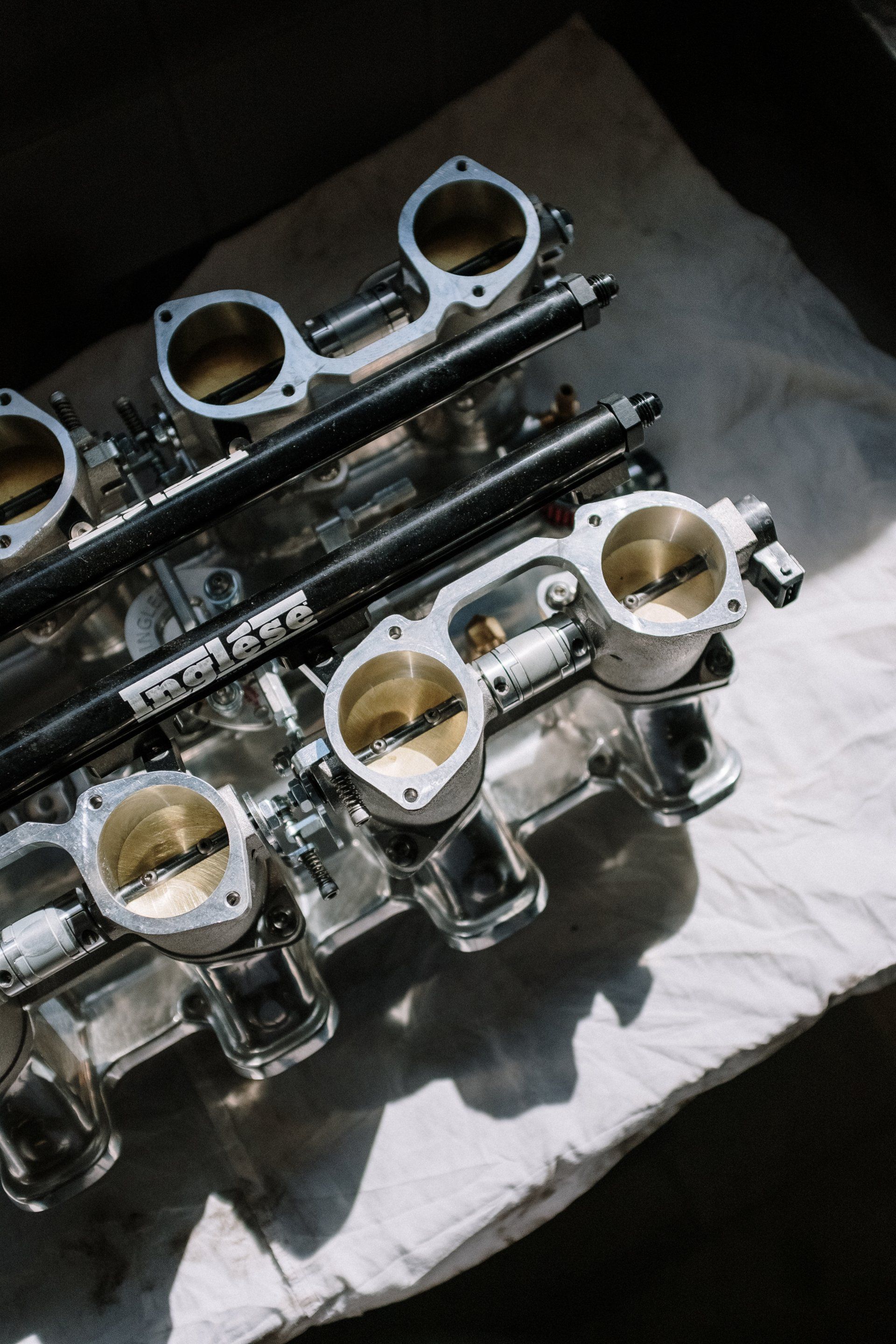Polished, multi-throttle intake manifold, likely for a car engine. Features open butterfly valves, fuel rails, and mounting flanges.