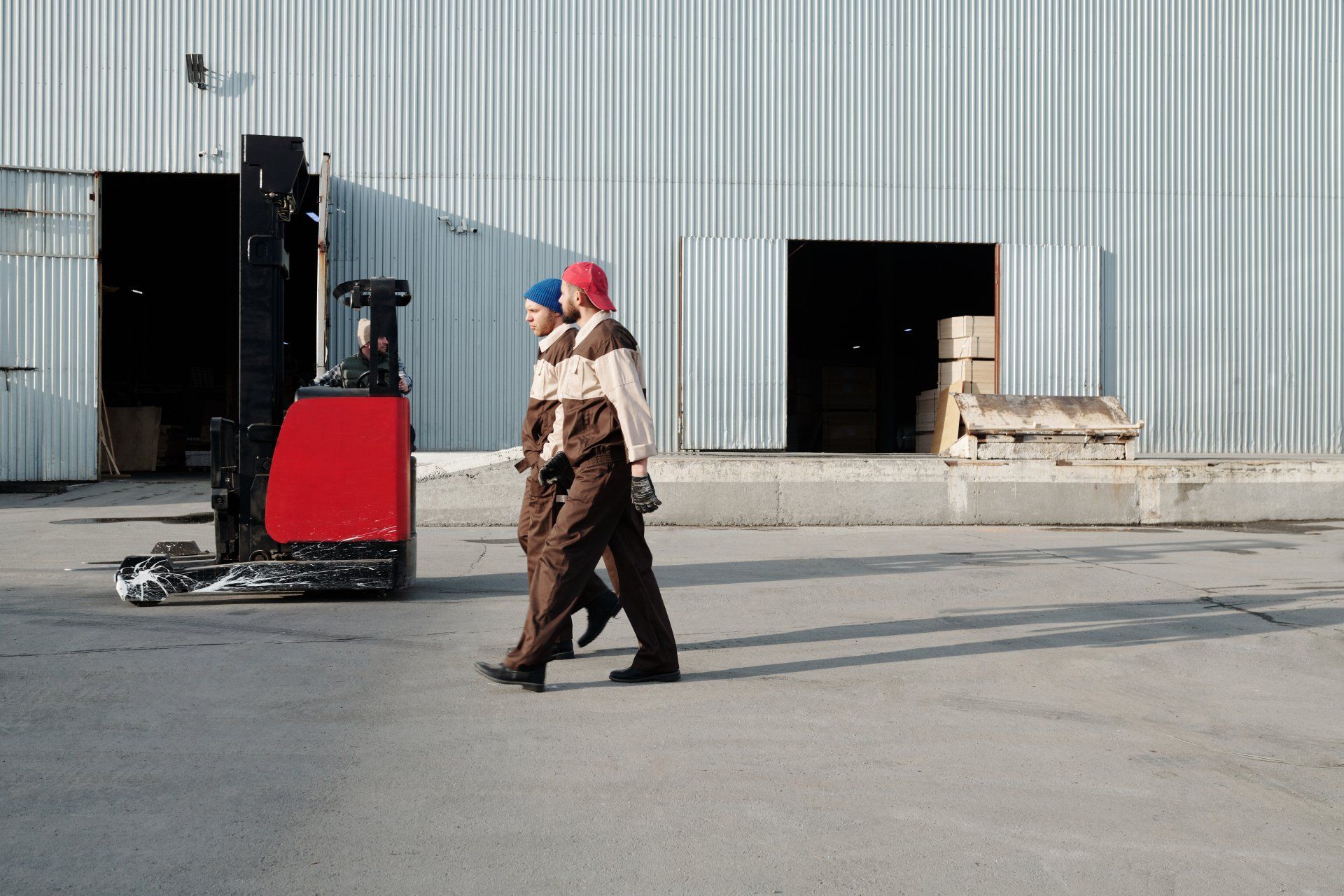 Two men are walking in front of a forklift in a warehouse.