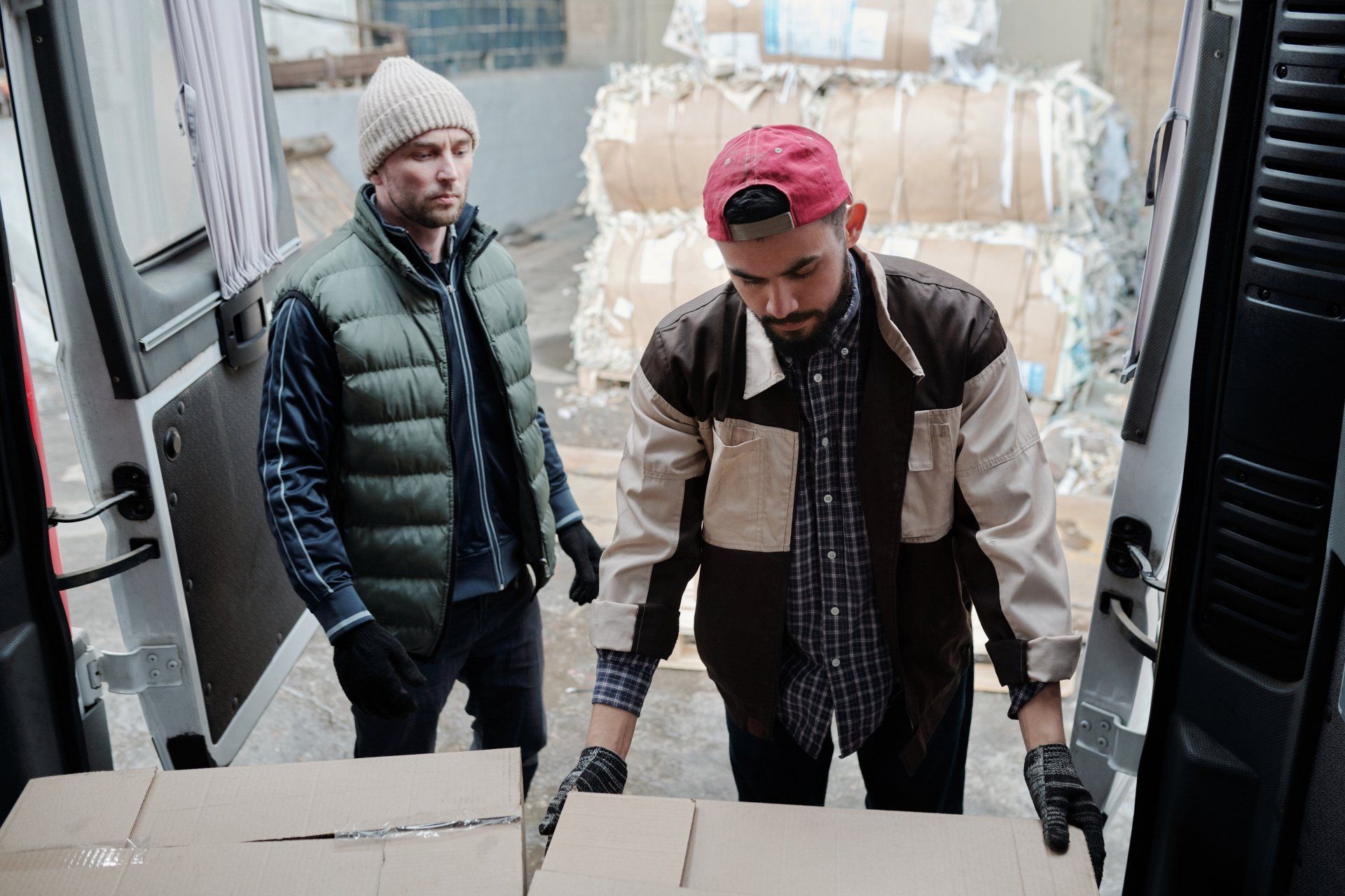 Two men are loading boxes into the back of a van.