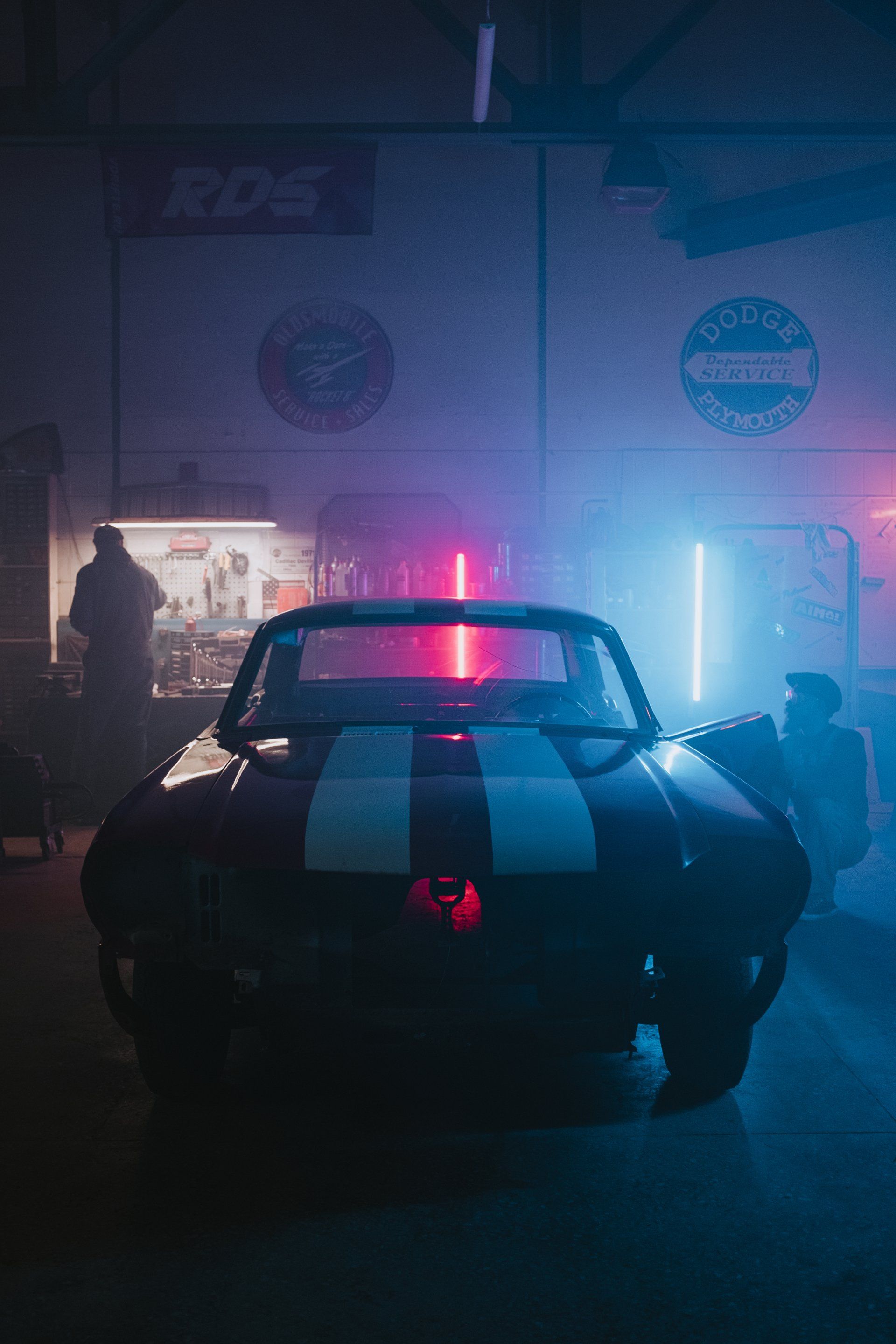 A man is standing next to a car in a garage at night.