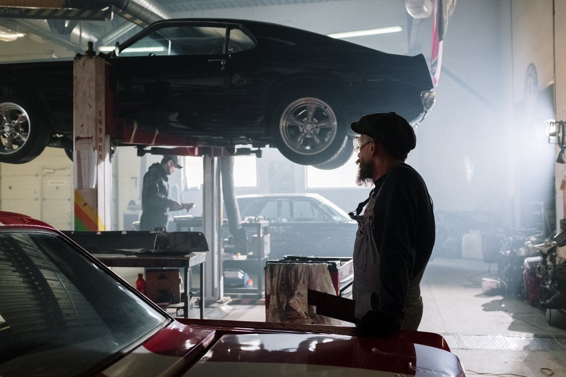 A man is standing in front of a car on a lift in a garage.