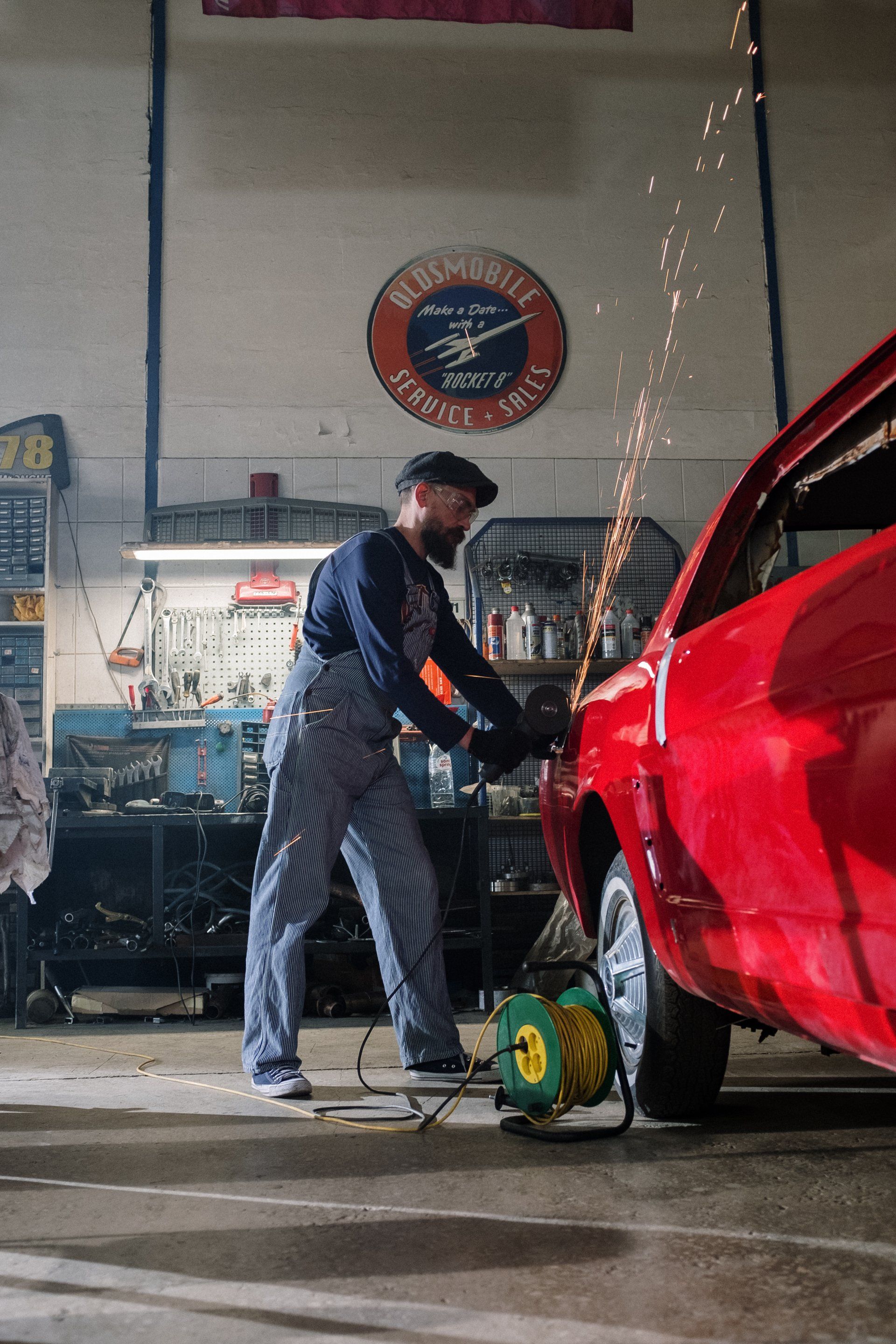 Man sawing the body of a red car in a workshop