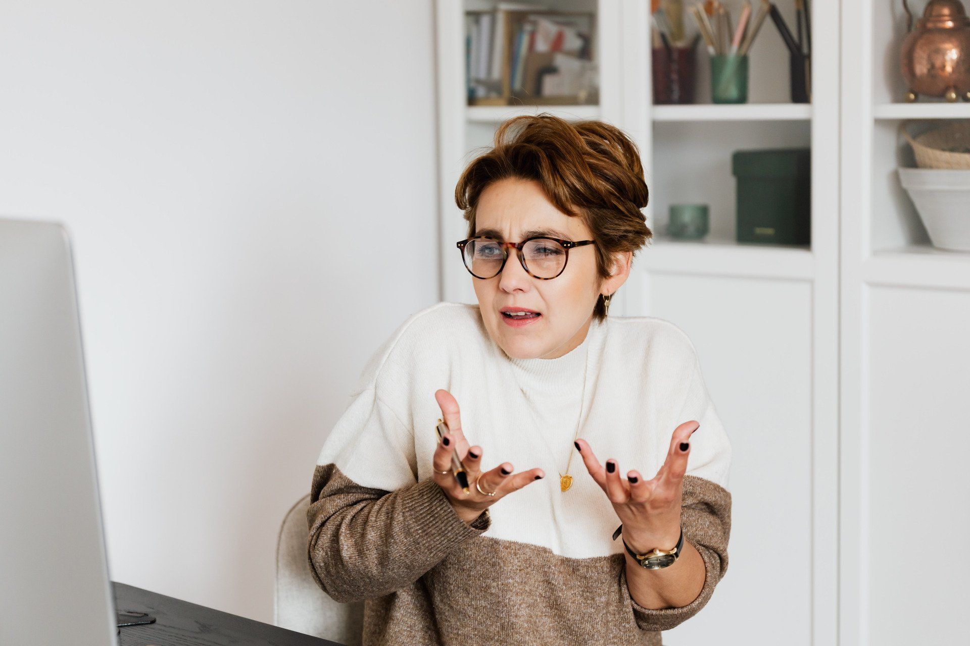Woman in a white scarf speaking with expressive hand gestures in a bright home office