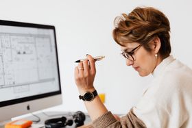A woman is sitting at a desk in front of a computer holding a pen.