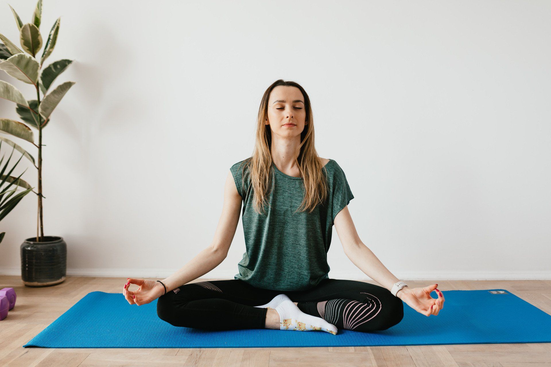 A woman is sitting in a lotus position on a yoga mat with her eyes closed.