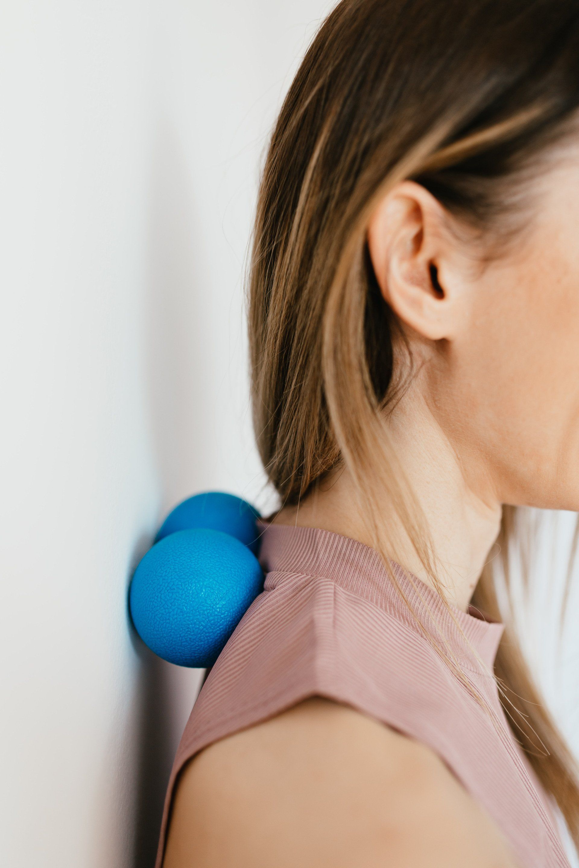 A woman is using a blue massage ball to massage her neck.