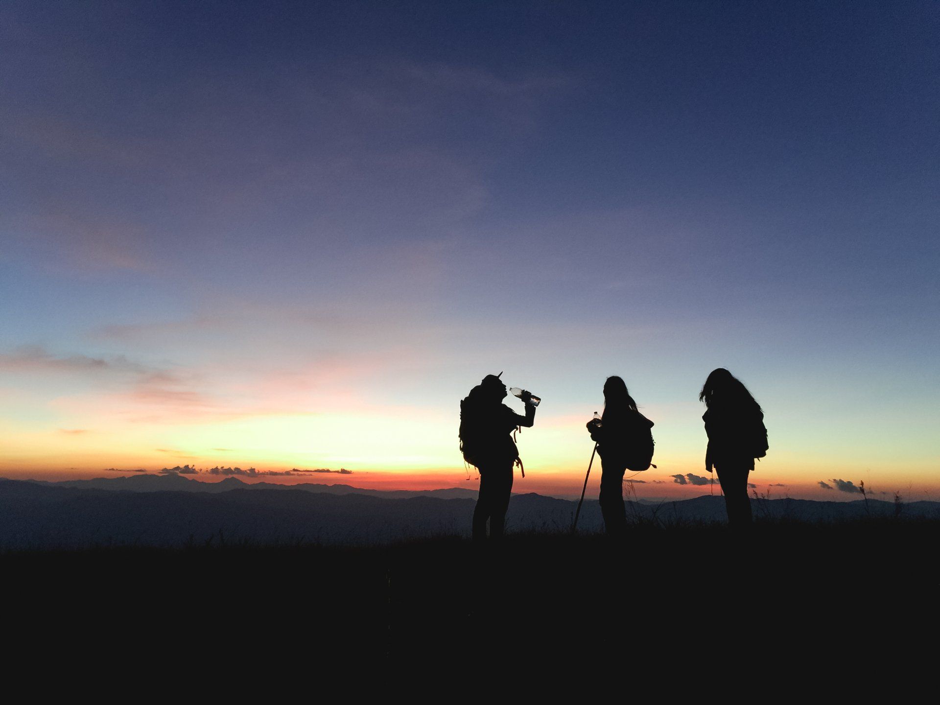 Three people standing on top of a hill at sunset