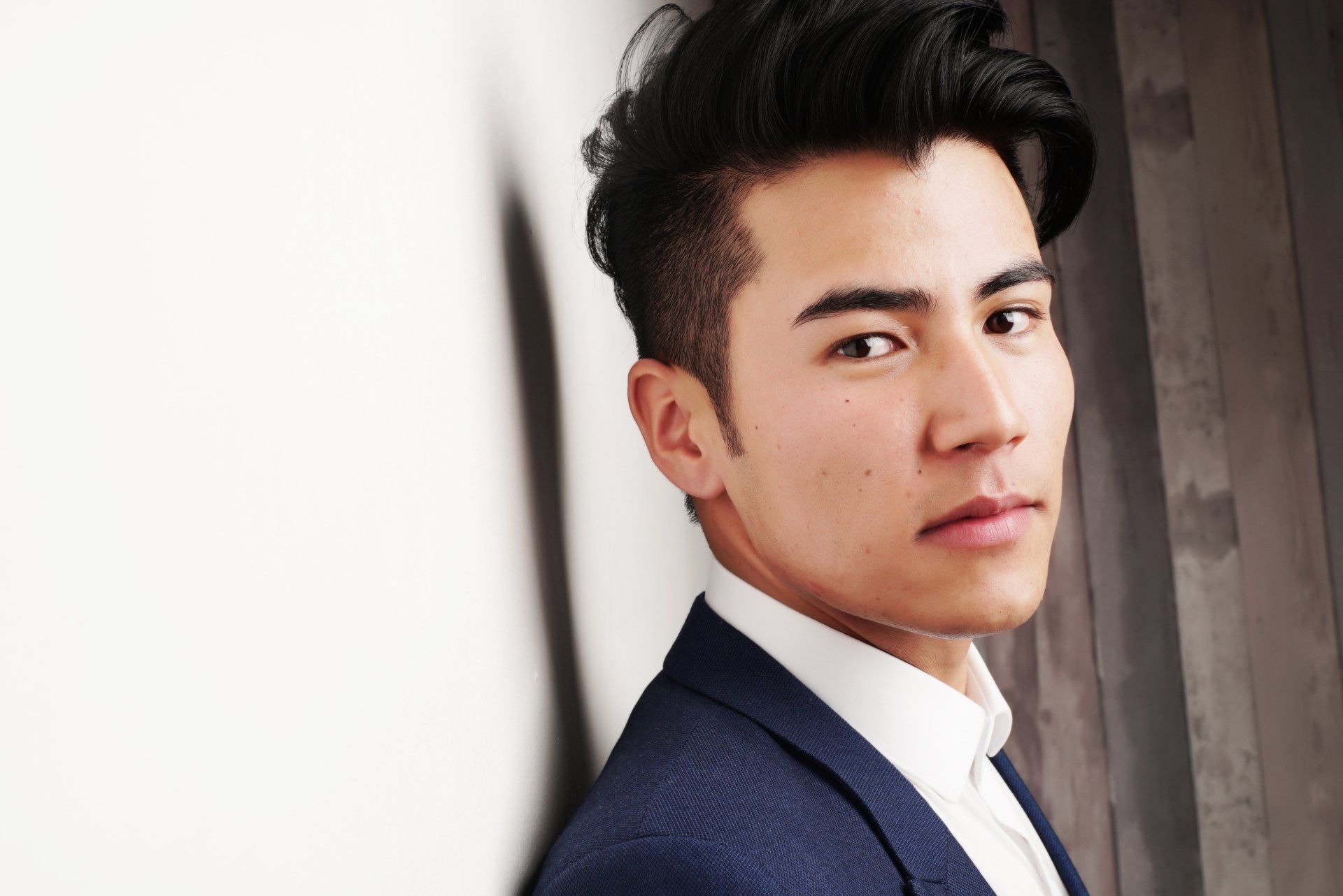 A man in a suit and tie is leaning against a wall.