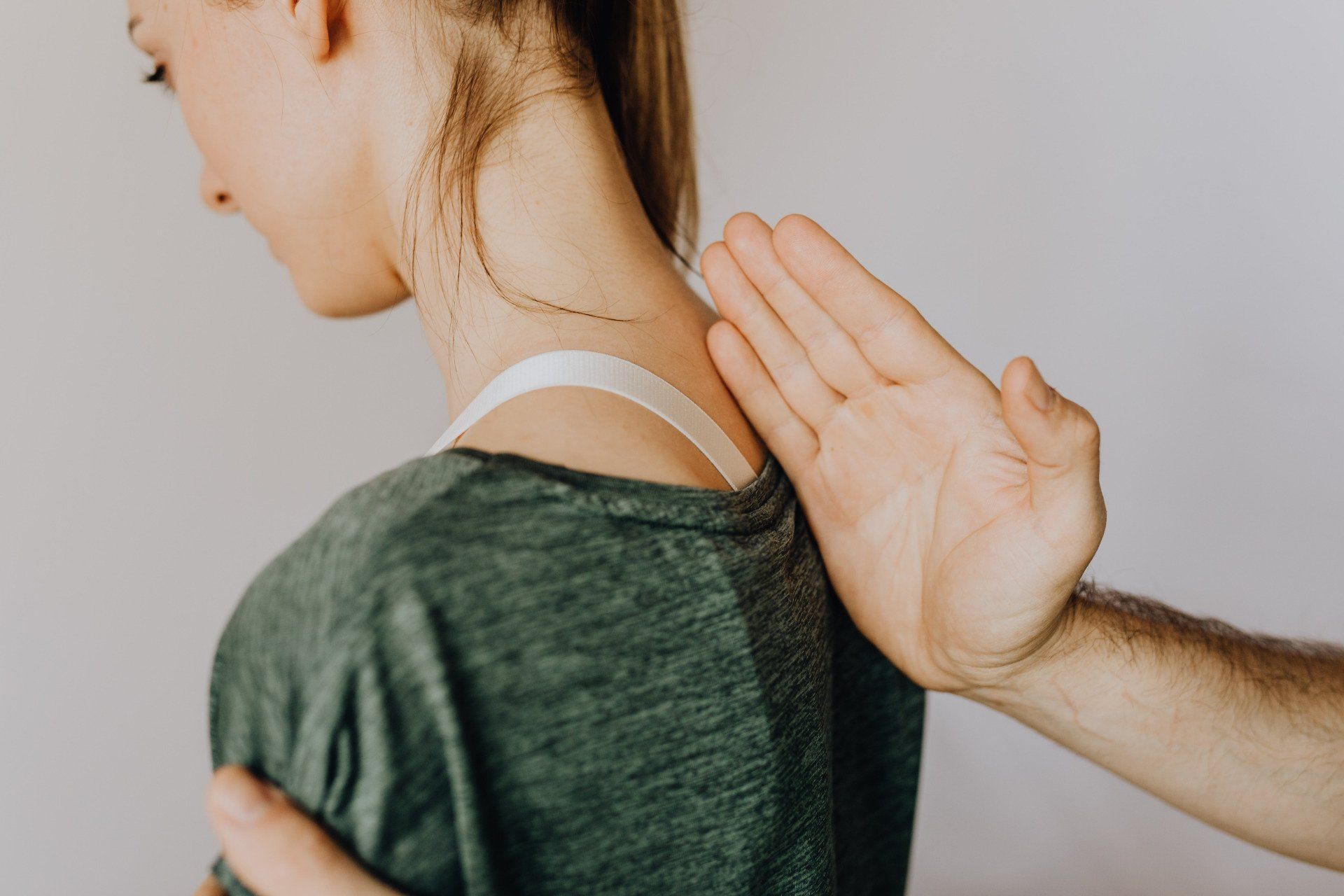 Person's back and neck being touched by a hand, possibly for a medical exam, against a white background.
