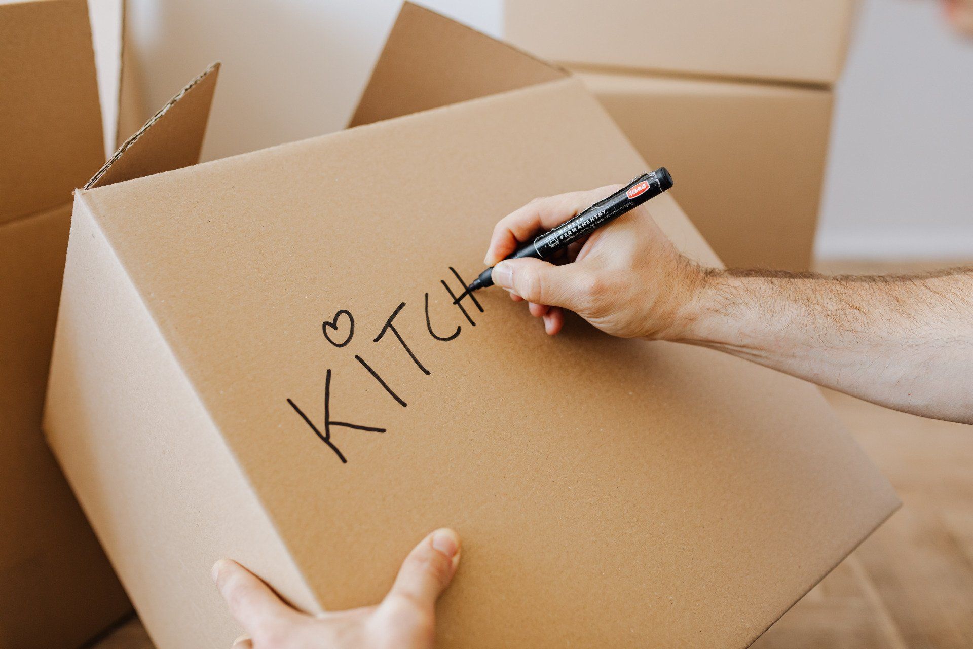 A person is writing the word kitchen on a cardboard box.
