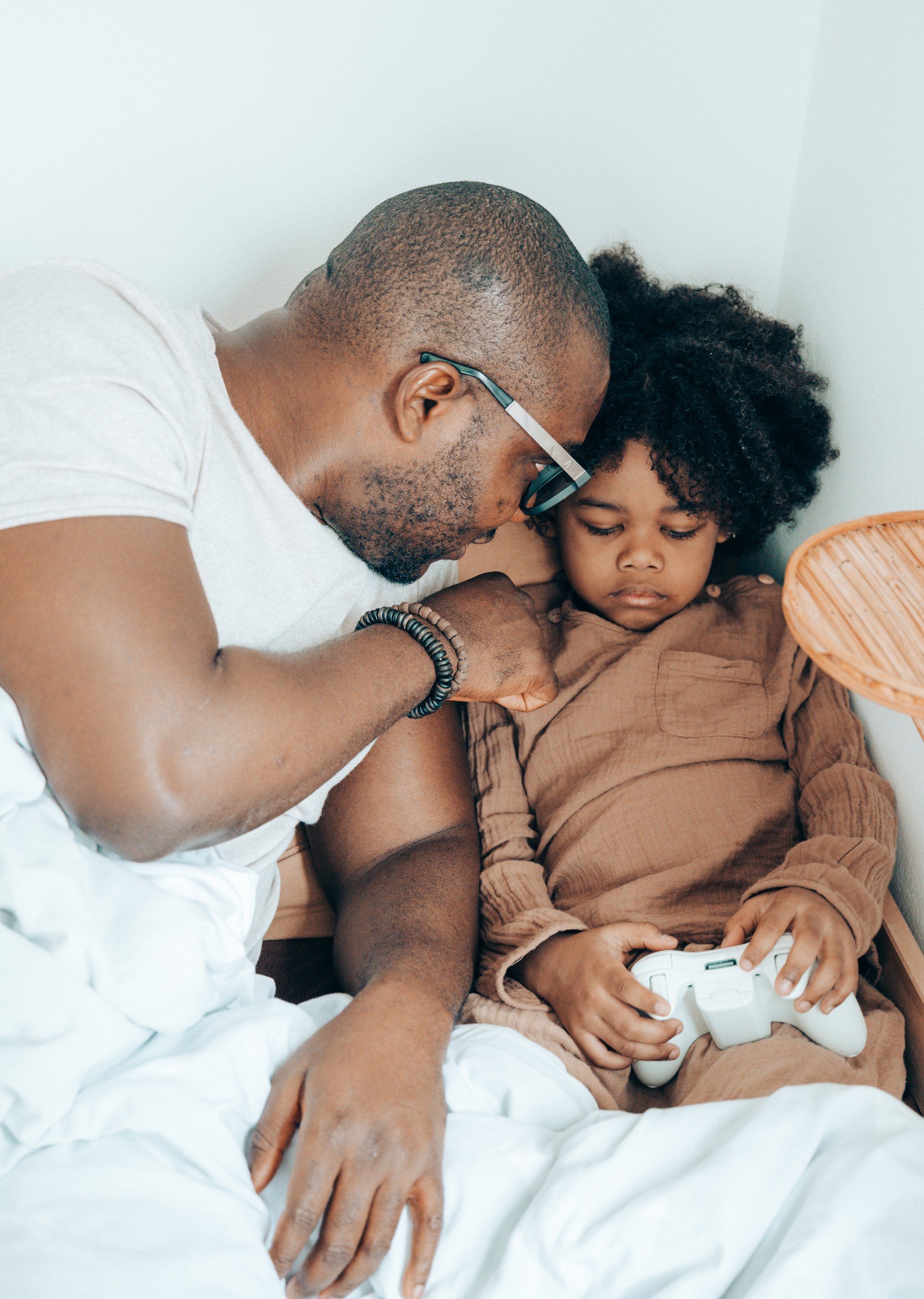 A man and a child are sitting on a bed playing a video game.