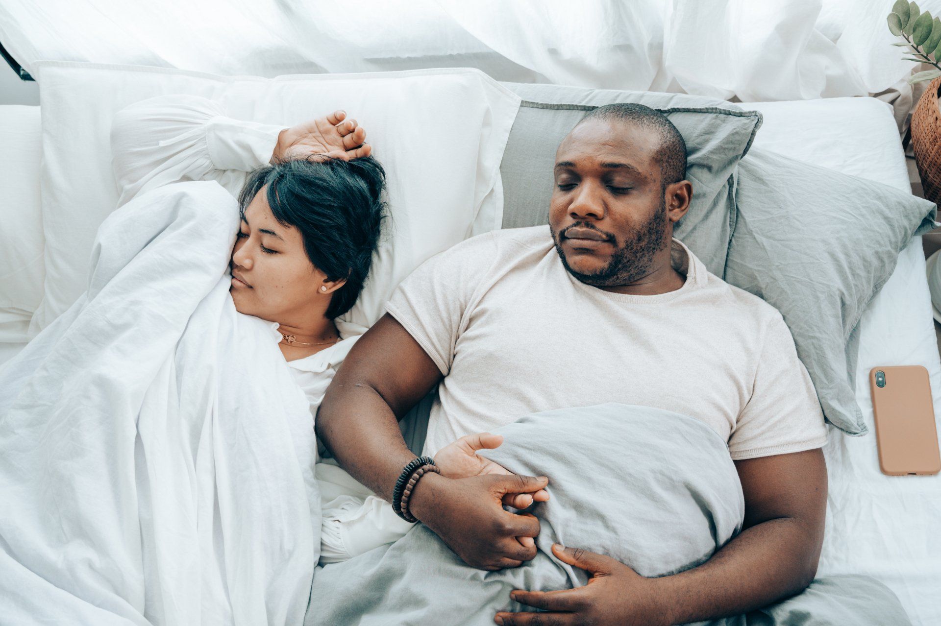 Couple sleeping in bed, holding hands. Man is awake, woman is asleep.