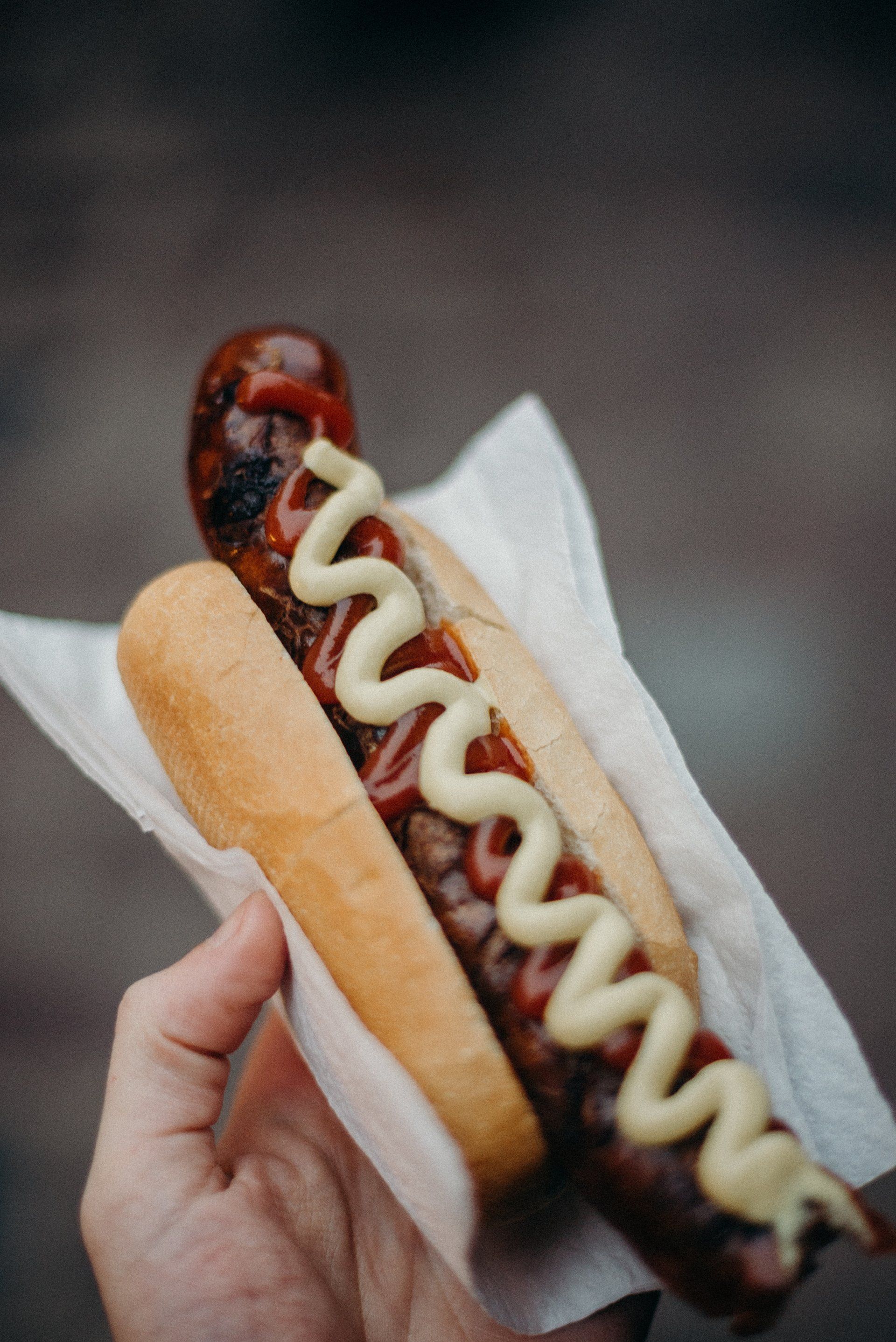 a person is holding a brat with ketchup and mustard on a napkin .