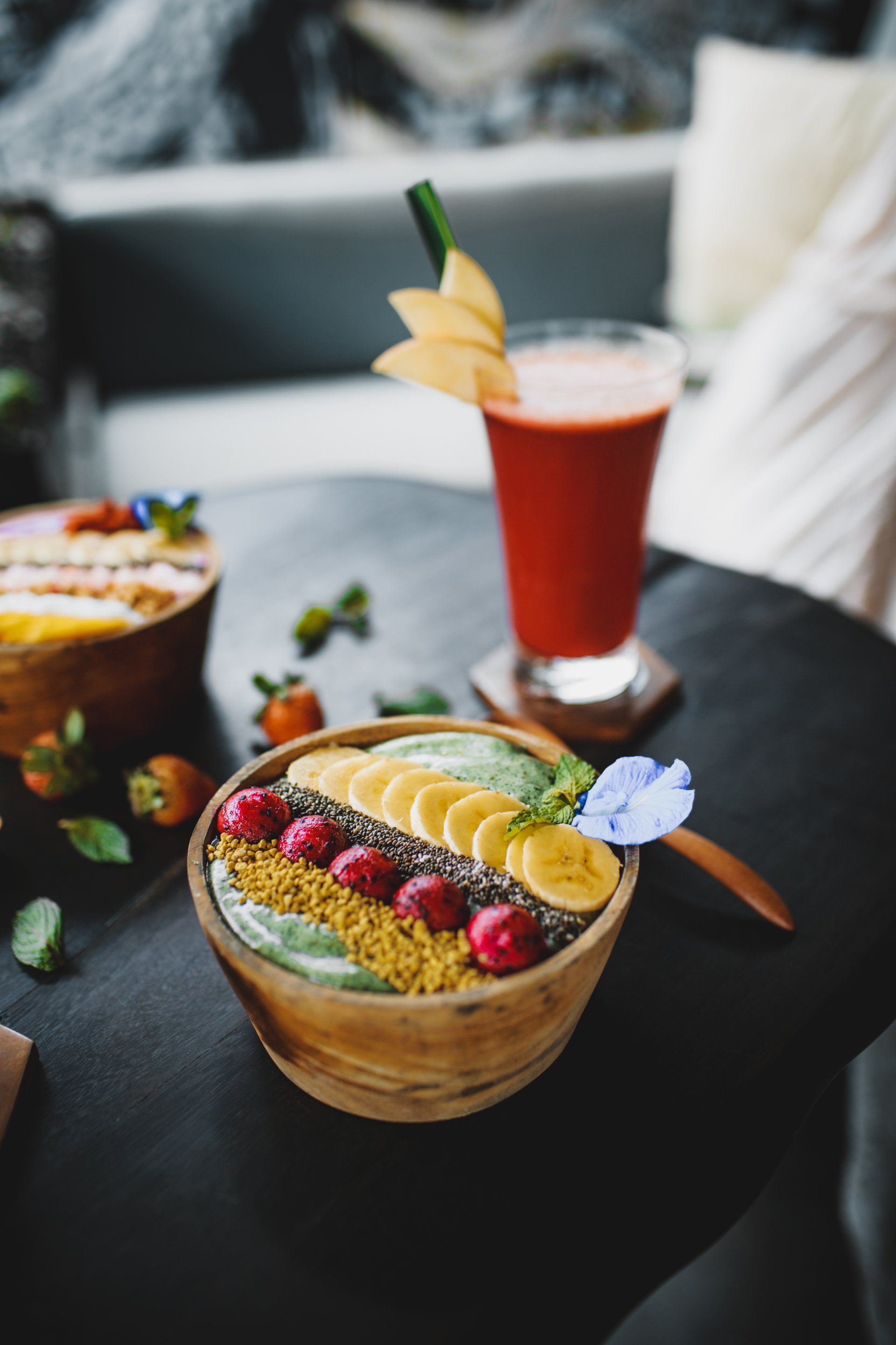 een schaal met fruit naast een glas sap op een tafel.