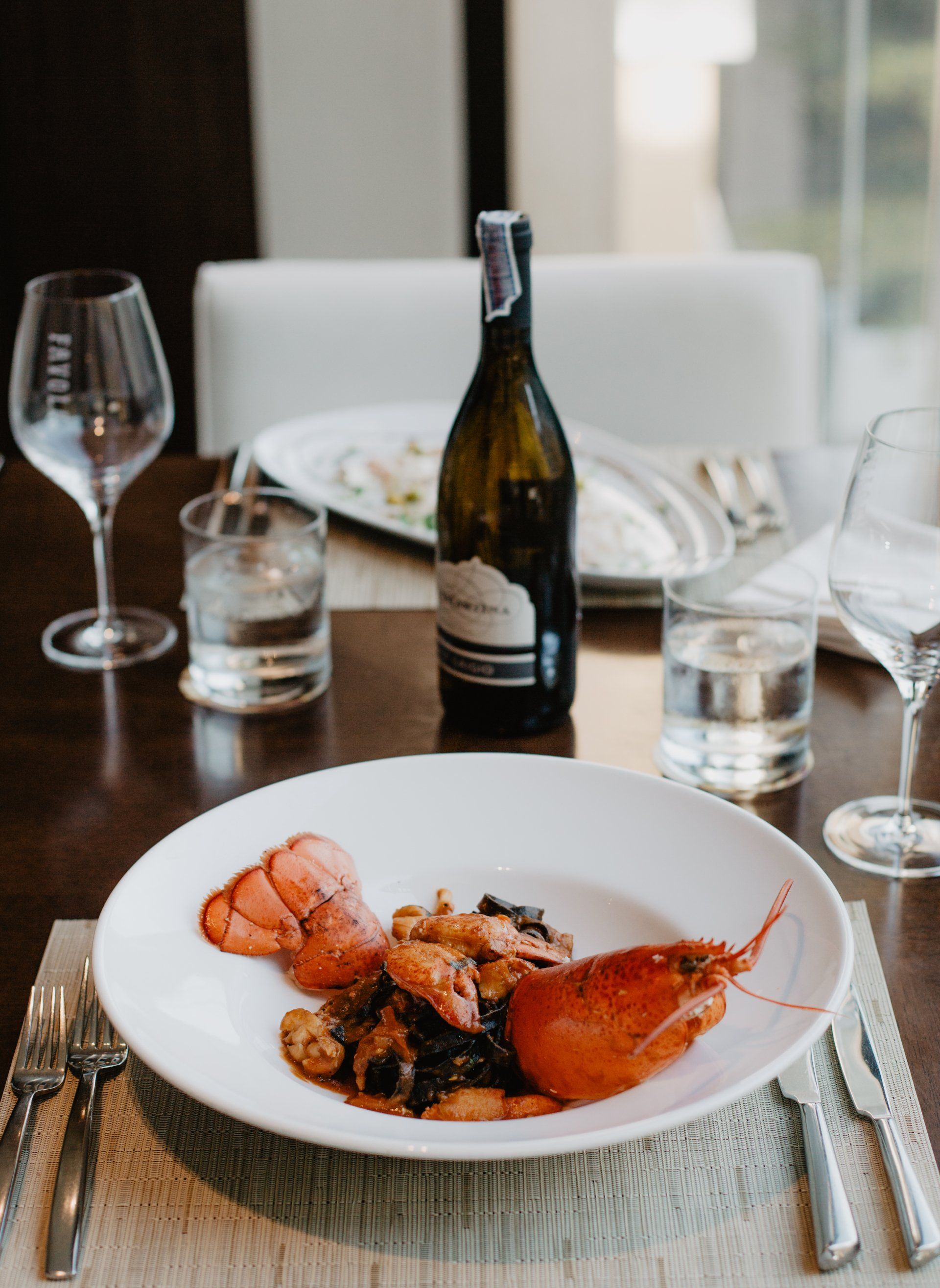 Plate of lobster and scallops on a dining table set with wine glasses and a bottle