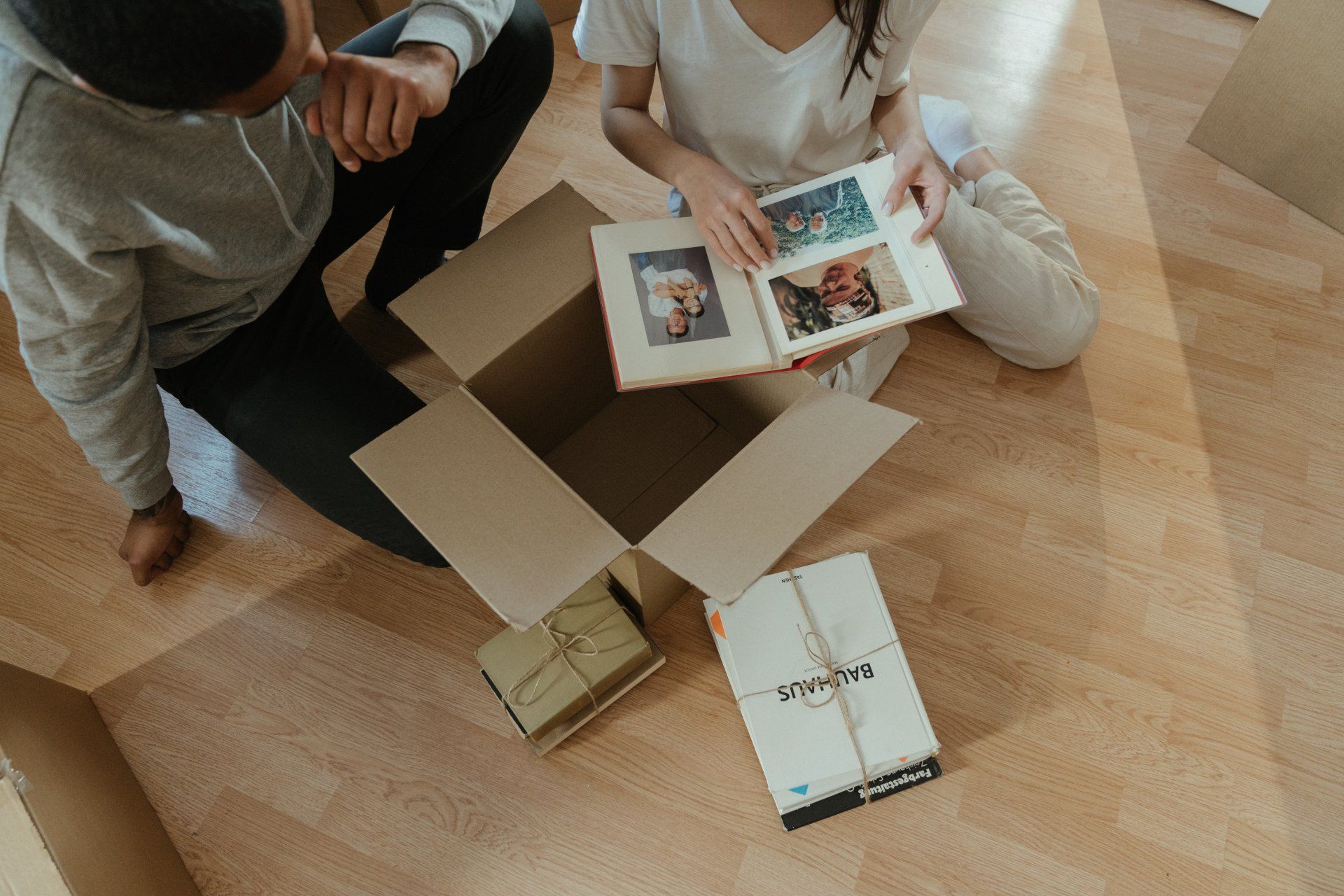 A man and a woman are sitting on the floor looking at a photo album.