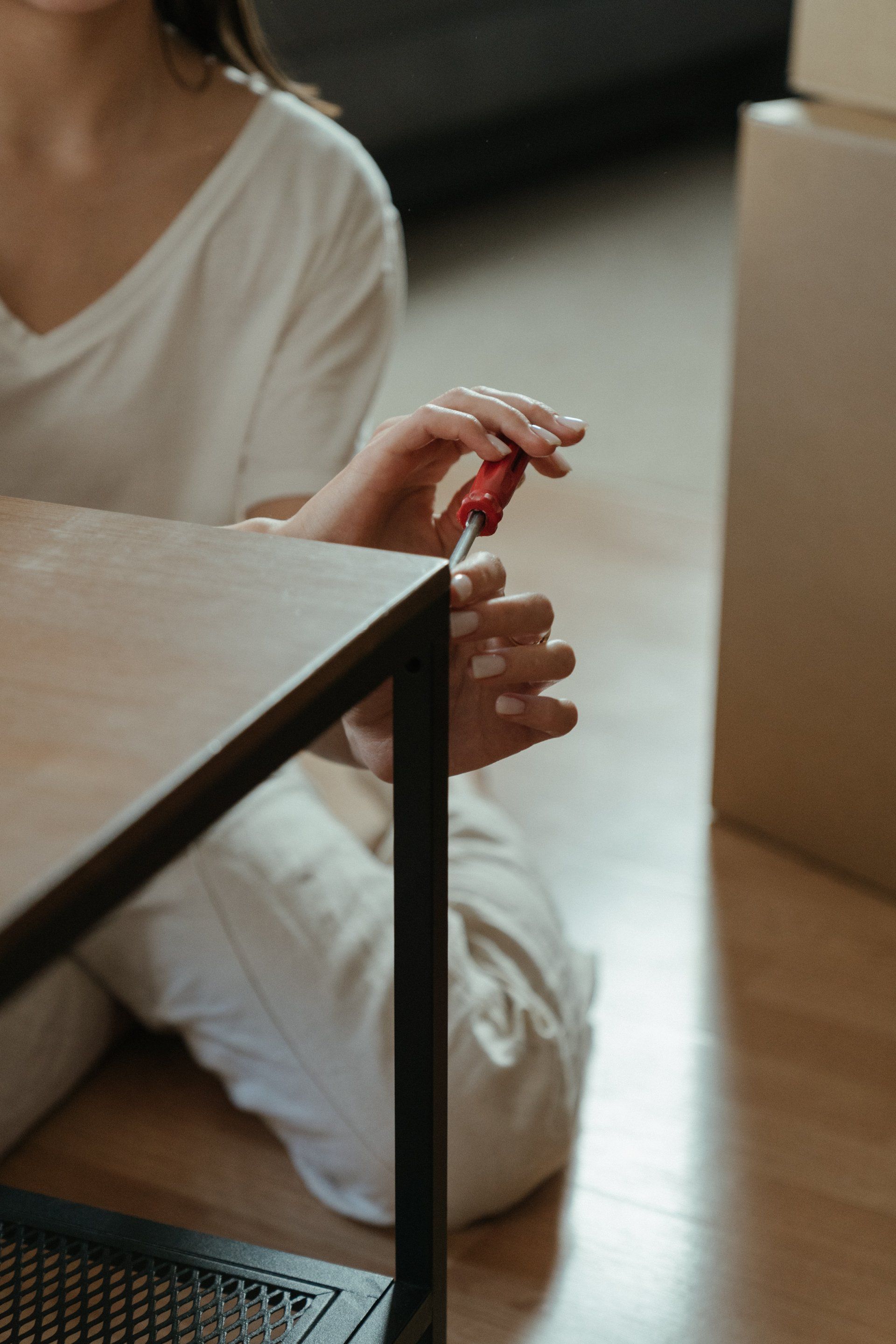 Woman assembling furniture with a red screwdriver, sitting on the floor.