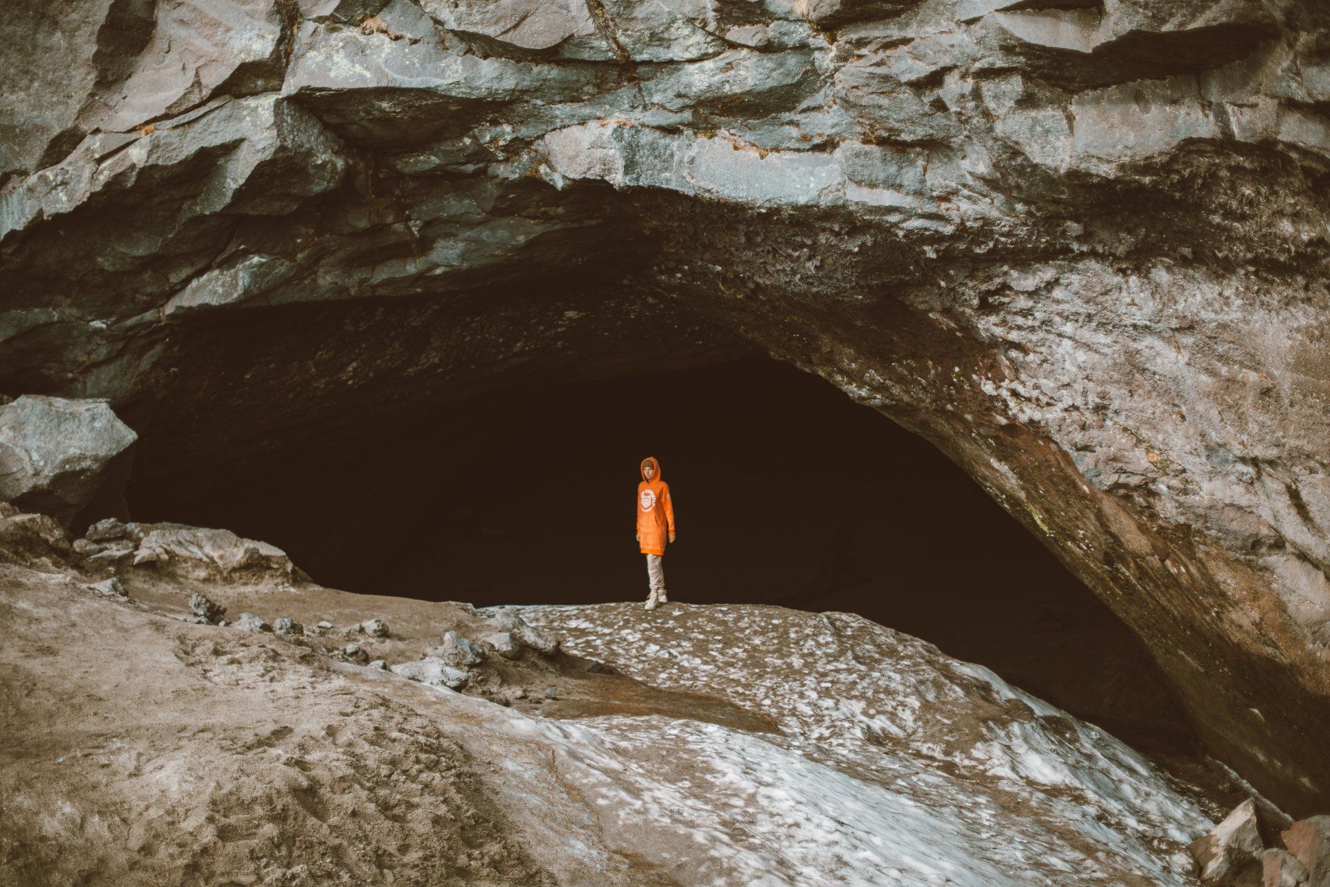 A person in an orange jacket is standing in a cave.