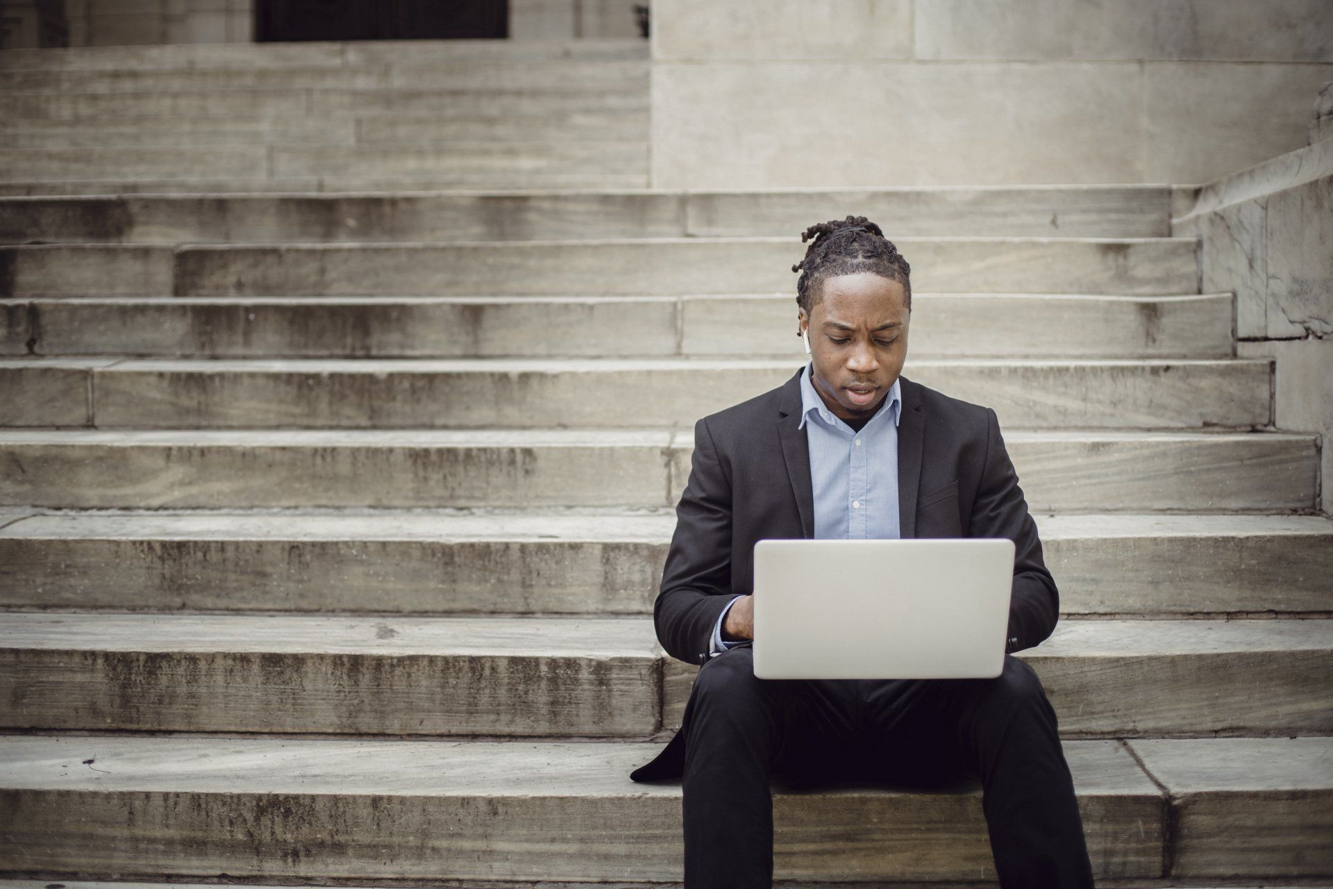 A man in a suit works on a laptop while sitting on stone steps.