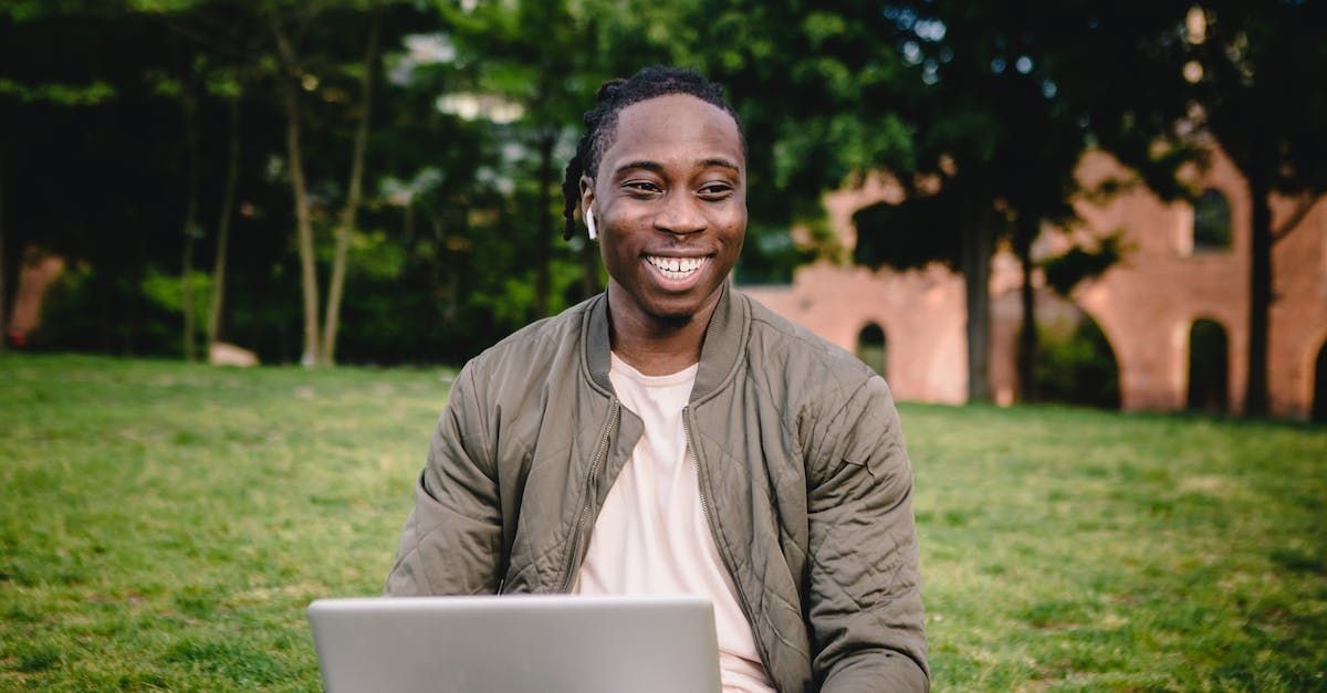 A man is sitting on the grass using a laptop computer.