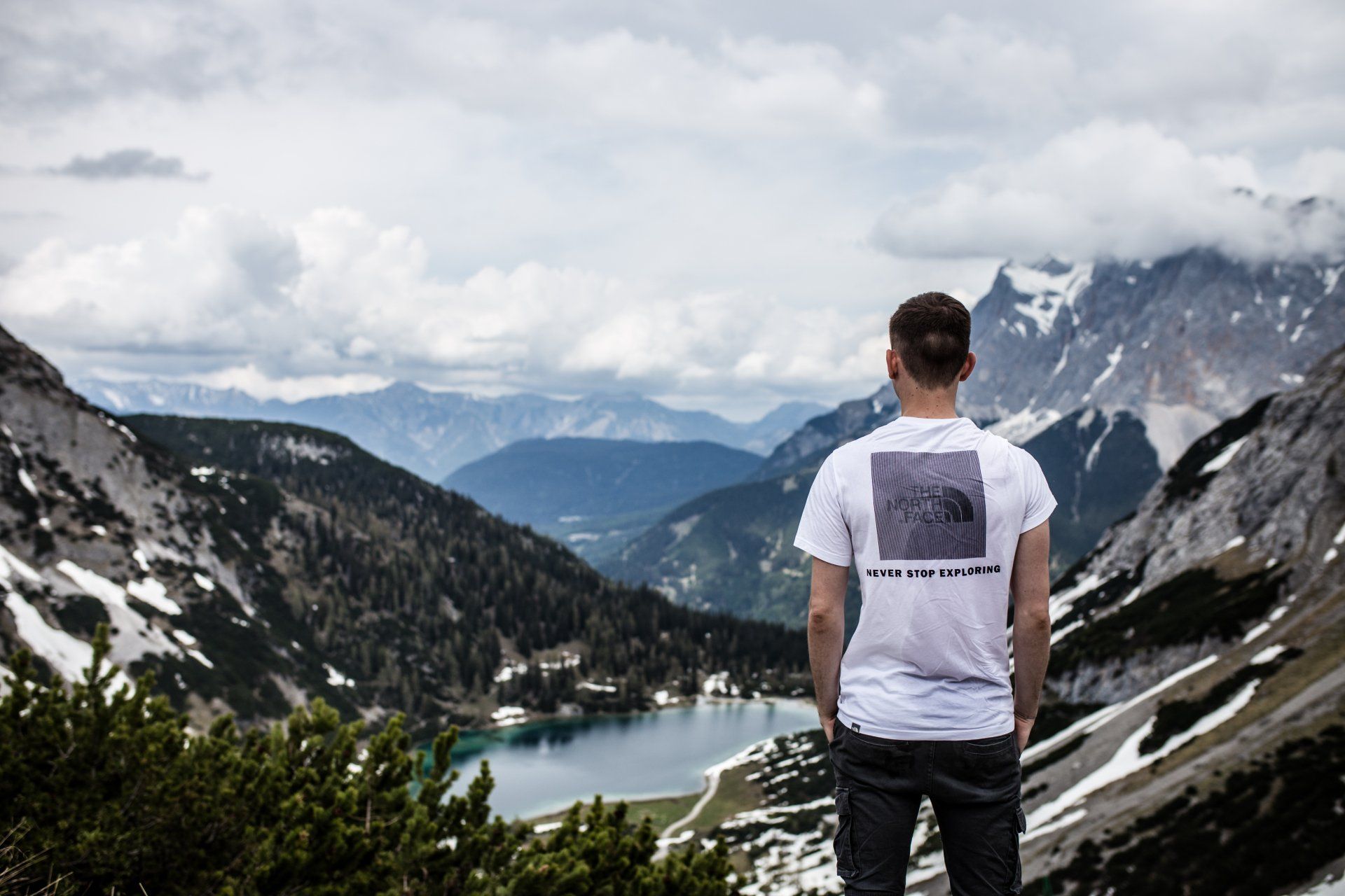 Ein Mann steht auf einem Berggipfel und blickt auf einen See