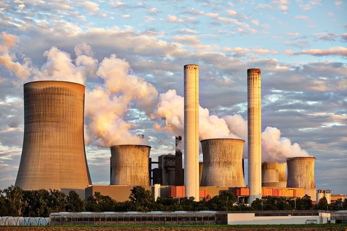Power plant with smoke stacks billowing fumes under a cloudy sky.